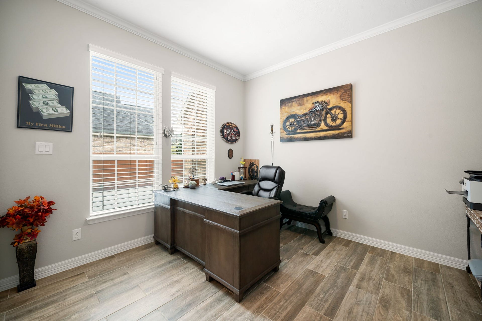 A private home office offers a quiet workspace with wood-look tile flooring and natural light from double windows.