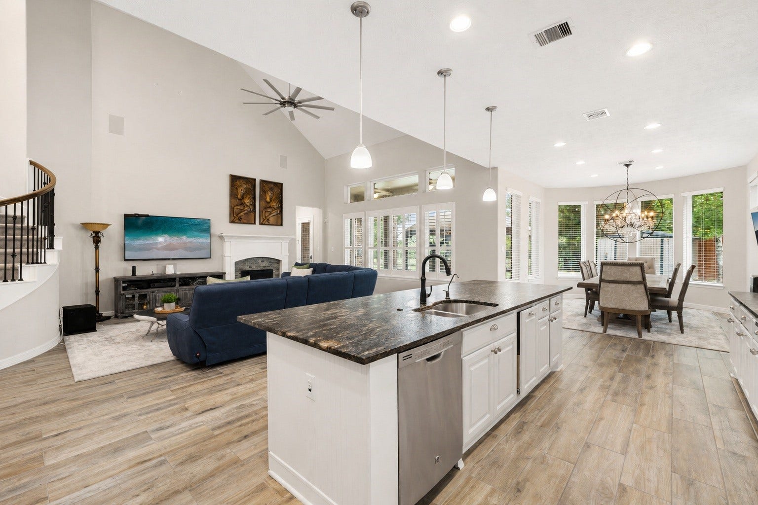 This view highlights the open flow from the kitchen into the living and dining areas, anchored by a large center island with seating space and views into the gathering room beyond. Virtually staged.