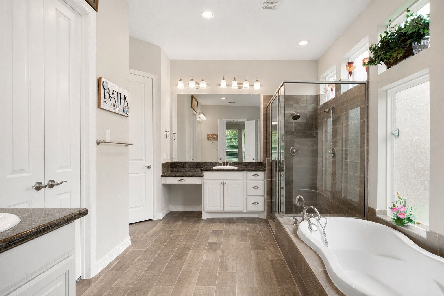 The primary bathroom features  granite-topped vanities, a separate walk-in shower, and a soaking tub framed by windows for a bright, spa-like feel.