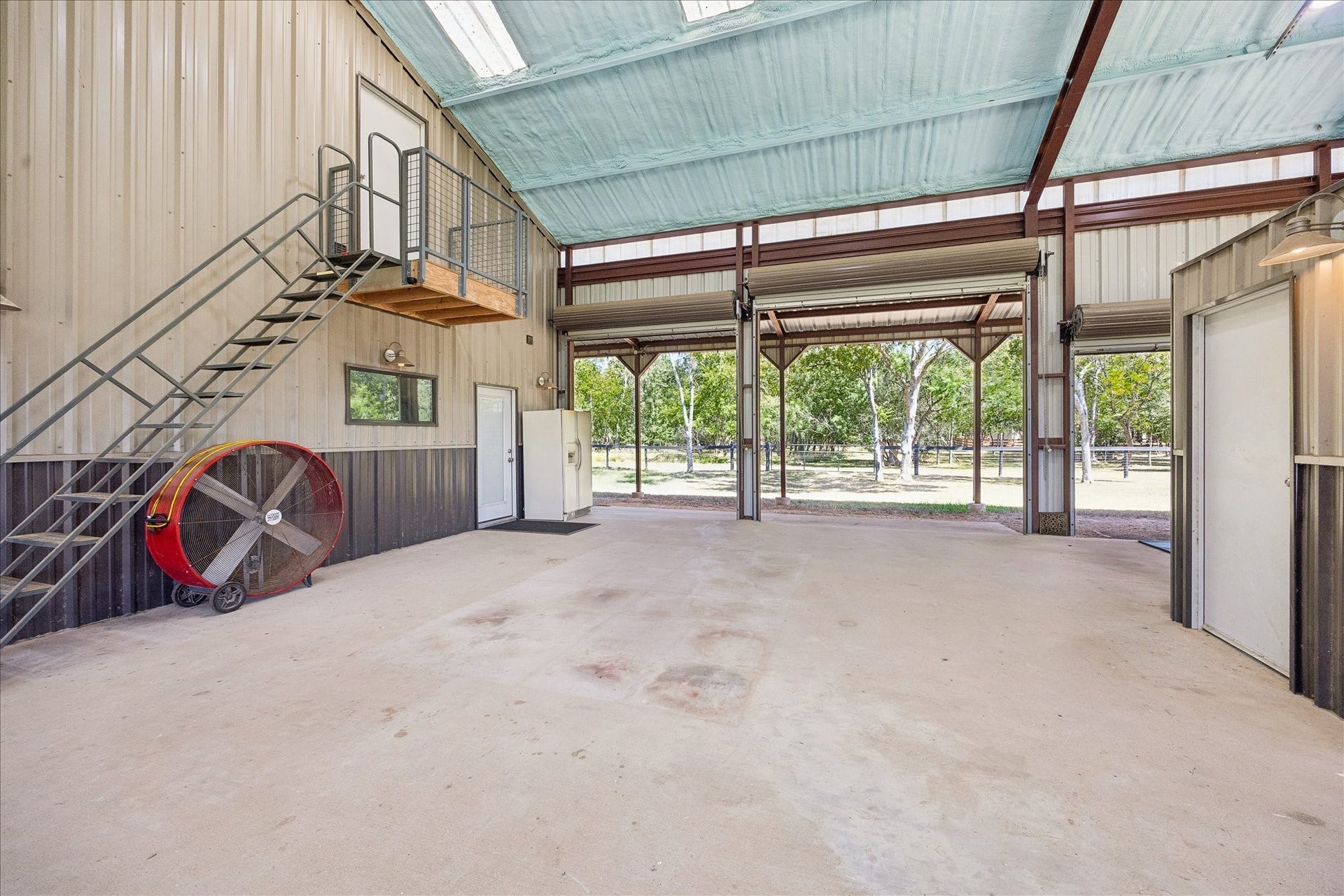 33 Riverwood Lane, Hempstead, TX 77445 This view of the open area shows the stairs to the attic and tack room on the right. There are 3 roll-up doors along that side of the covered area
