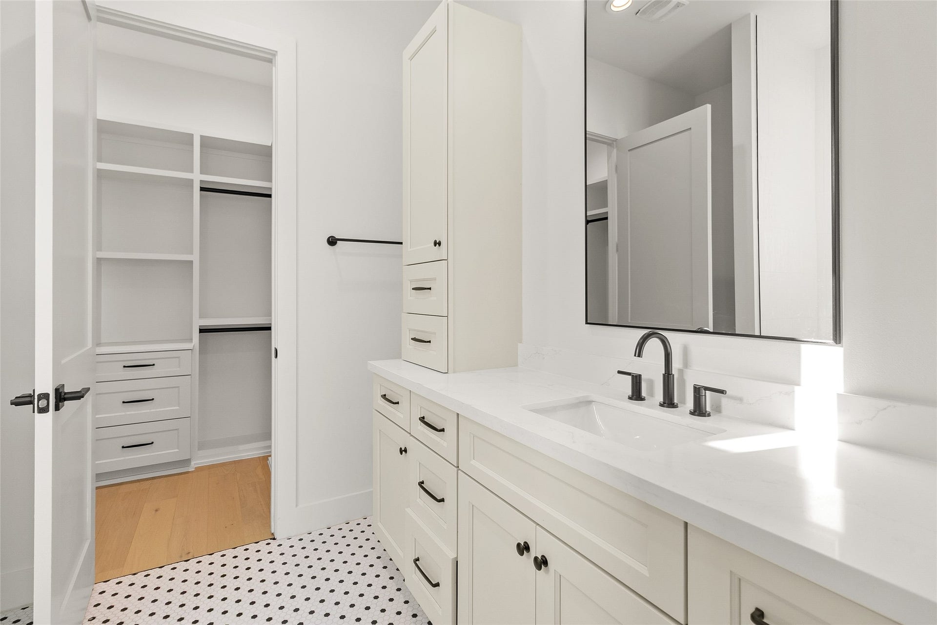 This well-appointed secondary bathroom pairs timeless style with everyday function. A spacious vanity topped with quartz counters offers ample storage, complete with a full-height cabinet tower and abundant drawers to keep everything organized. Classic black-and-white penny tile flooring adds a charming, characterful touch, while sleek matte black fixtures and hardware deliver a clean, modern contrast.