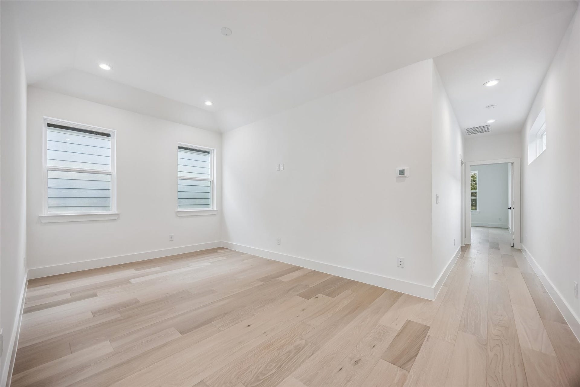 Bright and spacious room with light wood flooring, recessed lighting, and large windows offering plenty of natural light.