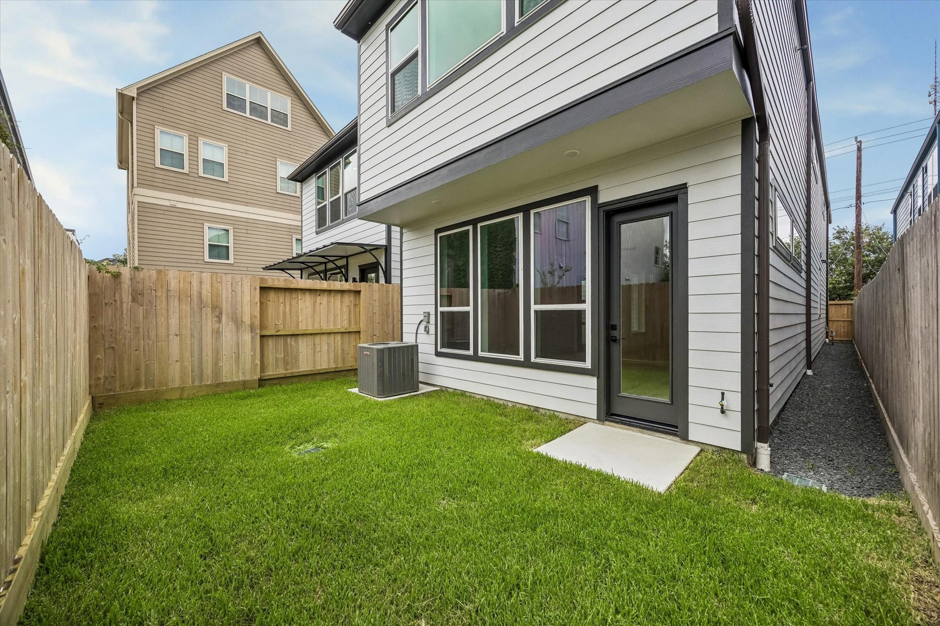 Charming backyard featuring a well-maintained lawn, private fencing, and a modern exterior with large windows and a sleek back door for easy outdoor access.