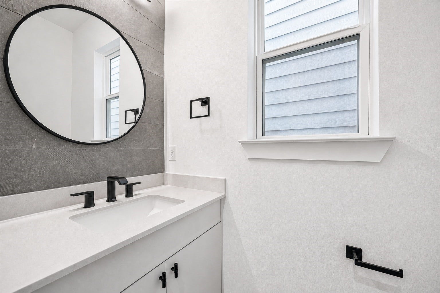 Modern bathroom featuring a sleek vanity with a round mirror, contemporary fixtures, and ample natural light from the window.