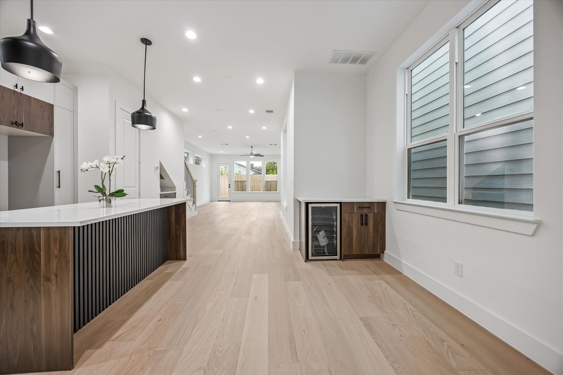 Modern open-concept living area featuring sleek wood floors, contemporary pendant lighting, and a spacious kitchen island with elegant finishes.