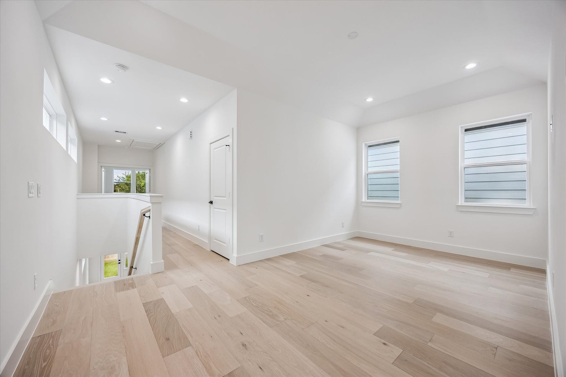 Bright and airy upper landing with light wood flooring, recessed lighting, and abundant natural light from multiple windows, ideal for a cozy reading nook or office space.