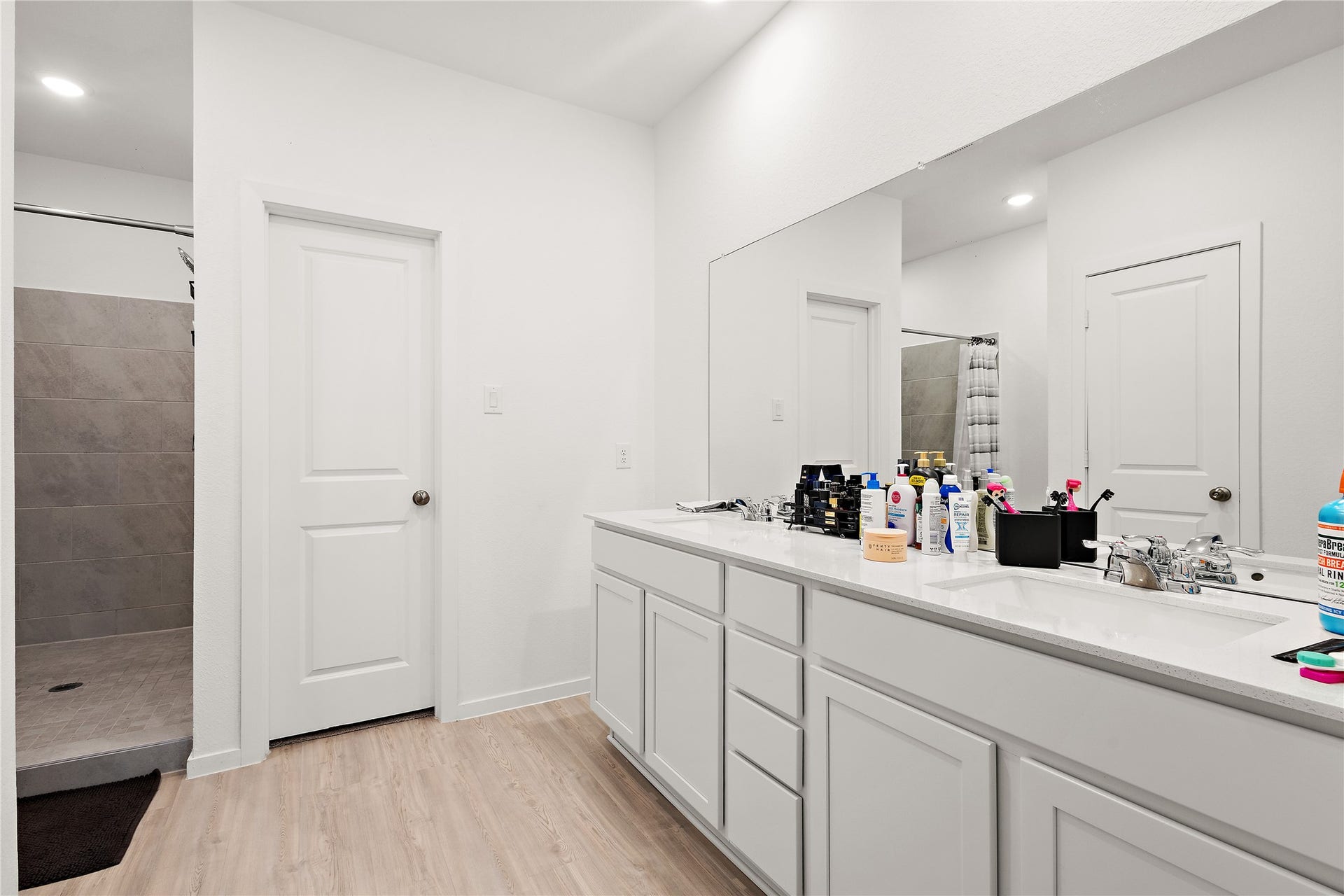 3414 Eden Valley Lane, Rosenberg, TX 77471 This bathroom features a modern design with a dual-sink vanity, ample counter space, and a large mirror. It has a walk-in shower with tiled walls and a sleek, light wood floor.