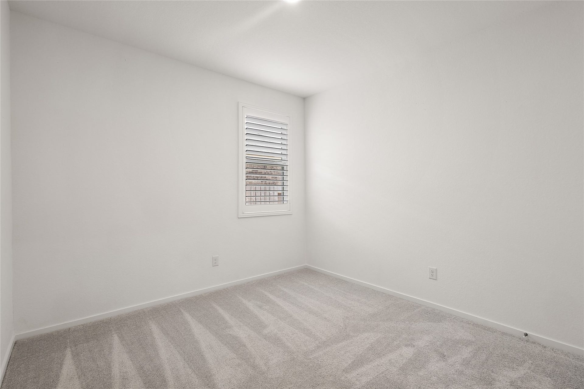 3414 Eden Valley Lane, Rosenberg, TX 77471 This photo shows a bright, small room with clean white walls and a light gray carpet. A window with shutters allows natural light to enter, creating a cozy atmosphere. Ideal for a home office or small bedroom.