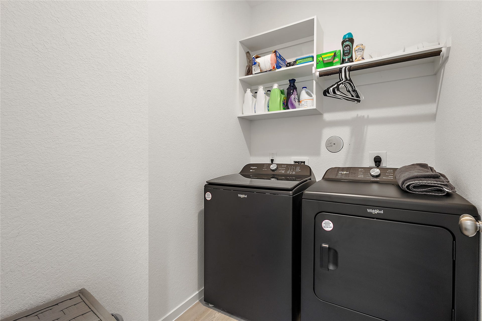 3414 Eden Valley Lane, Rosenberg, TX 77471 This is a compact, well-organized laundry room featuring a modern washer and dryer set, wall-mounted shelving for storage, and a hanging rod for clothes.