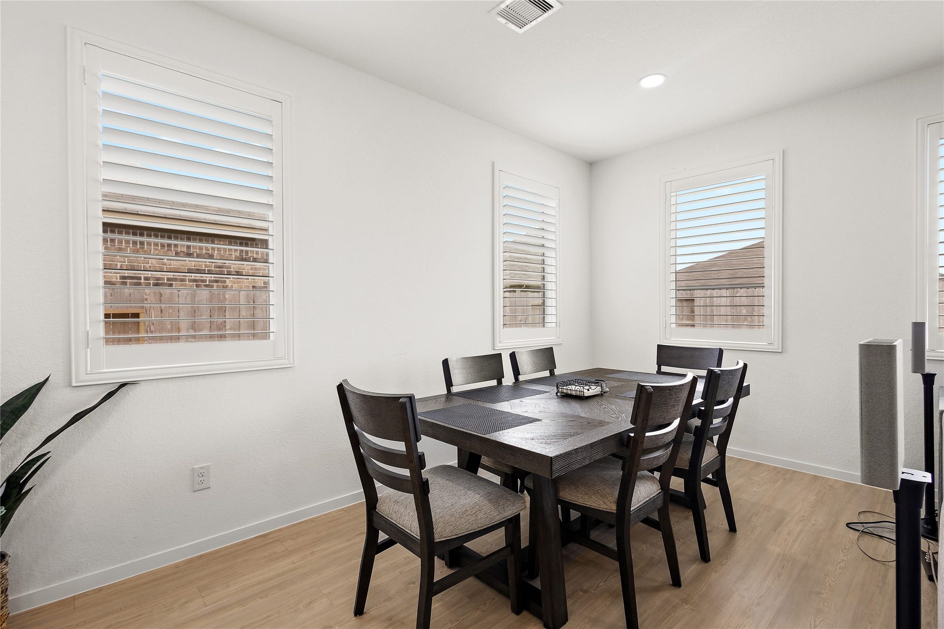 3414 Eden Valley Lane, Rosenberg, TX 77471 This dining area offers a bright, modern space with light wood flooring, white walls, and three large windows with shutters. It features a sleek dark wood table set for six, creating an inviting atmosphere for meals.