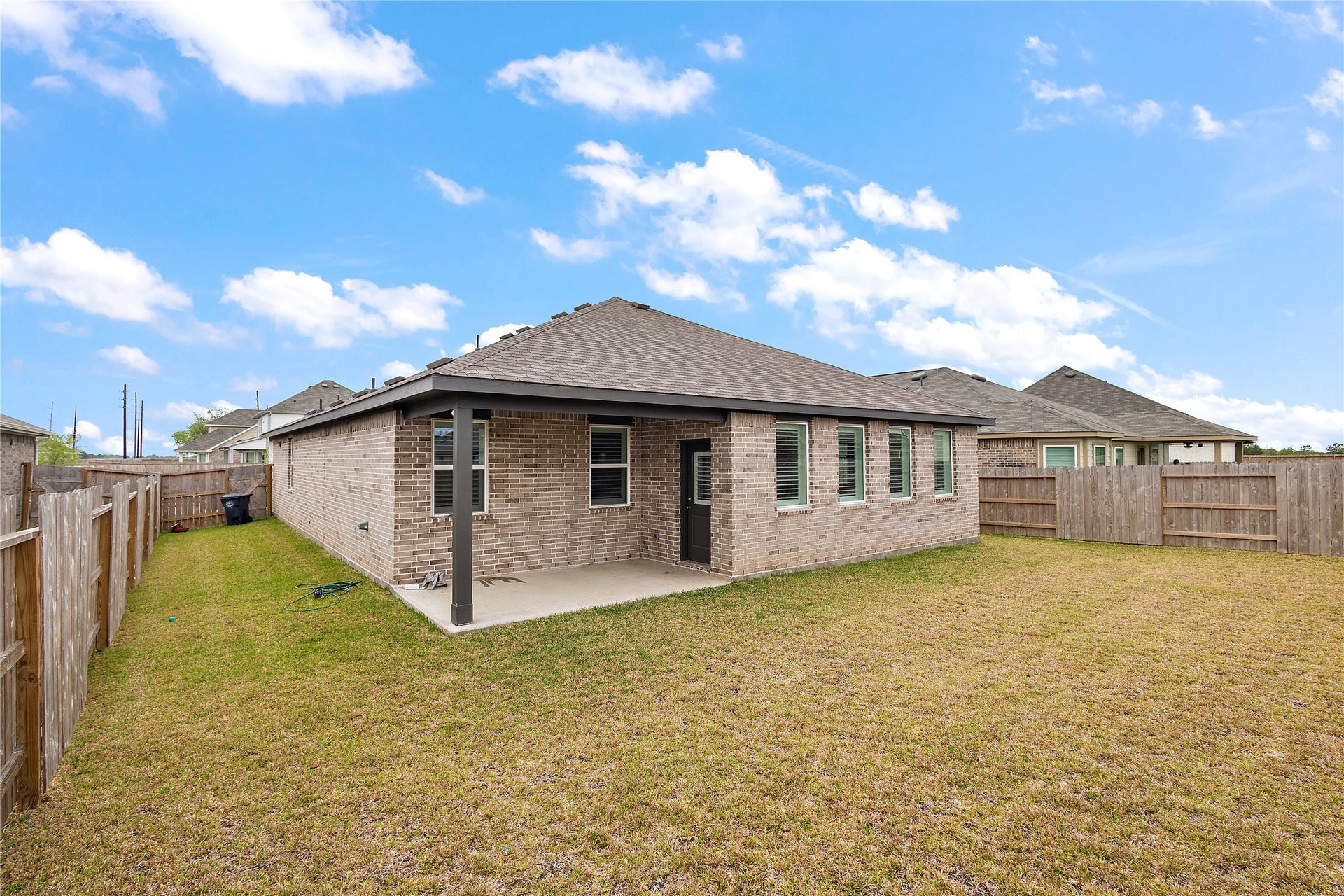 3414 Eden Valley Lane, Rosenberg, TX 77471 backyard with a brick house featuring a patio. The yard is spacious with a well-maintained lawn, and the house has multiple windows for natural light.