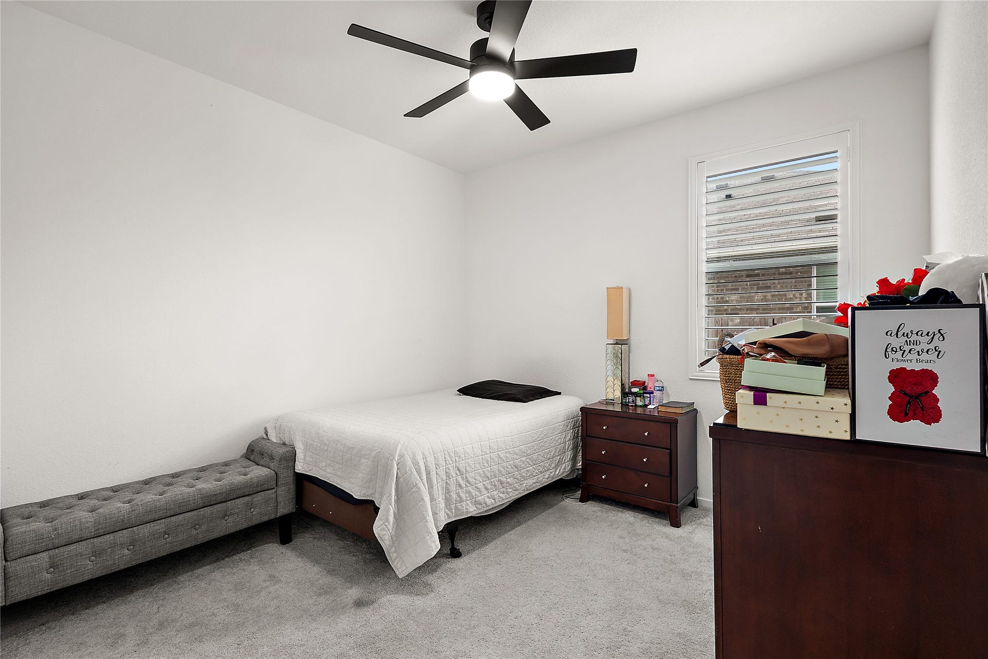 3414 Eden Valley Lane, Rosenberg, TX 77471 This cozy bedroom features a minimalist design with neutral colors, a ceiling fan, and a window for natural light. It includes a bed, a bench, and wooden dressers for storage.