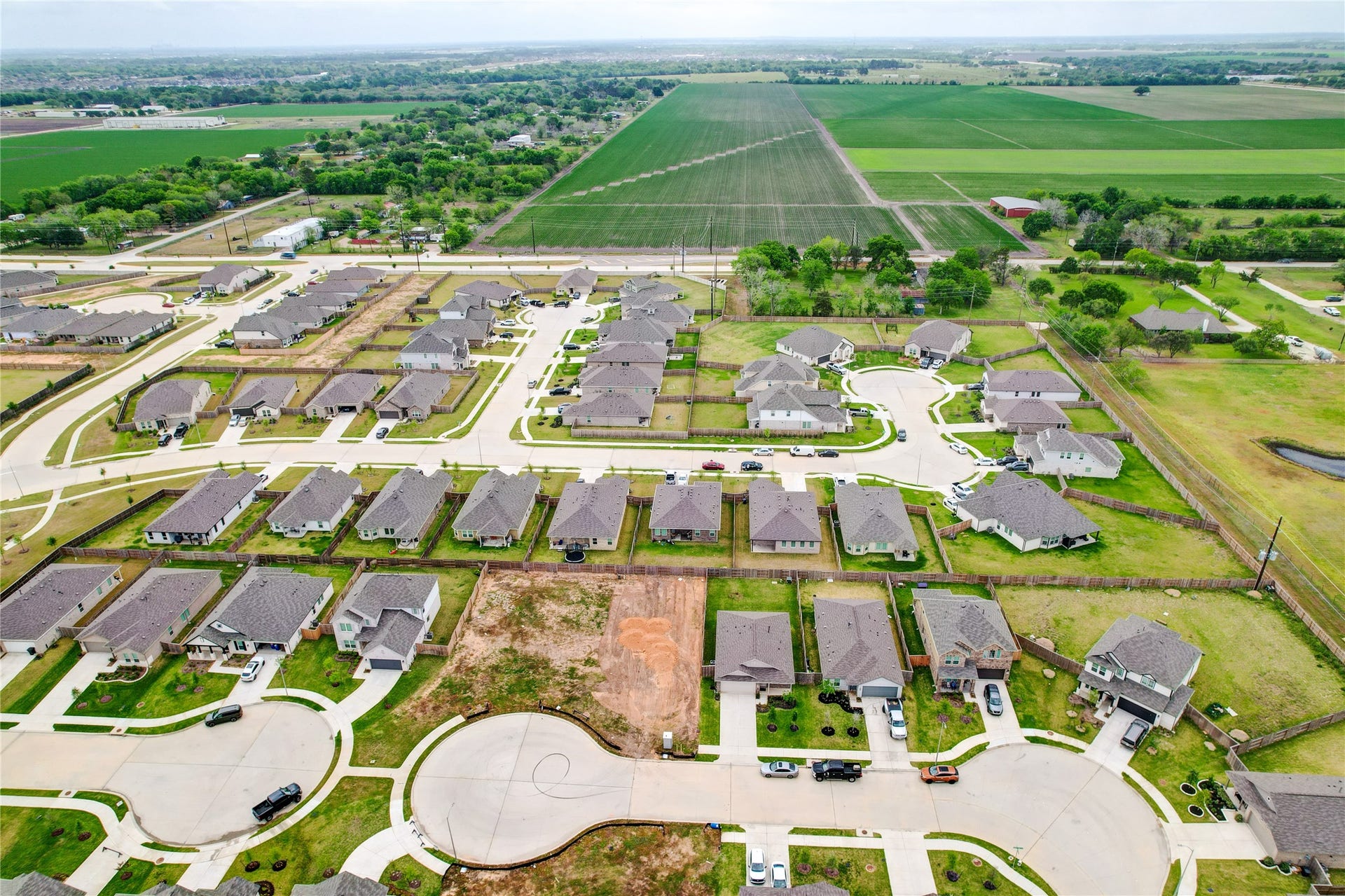 3414 Eden Valley Lane, Rosenberg, TX 77471 This aerial photo showcases a modern residential neighborhood with neatly arranged single-family homes, surrounded by open green fields. The community features well-maintained streets, cul-de-sacs, and ample yard space, offering a serene and spacious living environment.