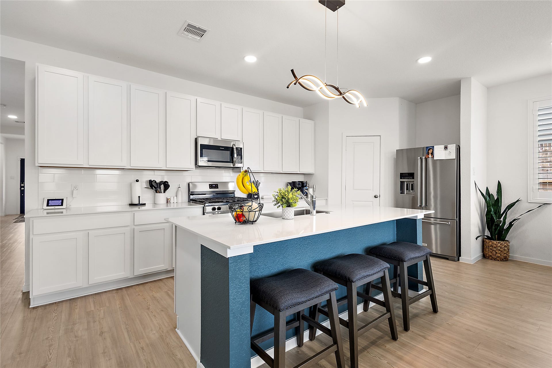3414 Eden Valley Lane, Rosenberg, TX 77471 Modern kitchen with sleek white cabinets, stainless steel appliances, and a spacious island with seating. The light wood flooring and contemporary lighting fixture add warmth and style.