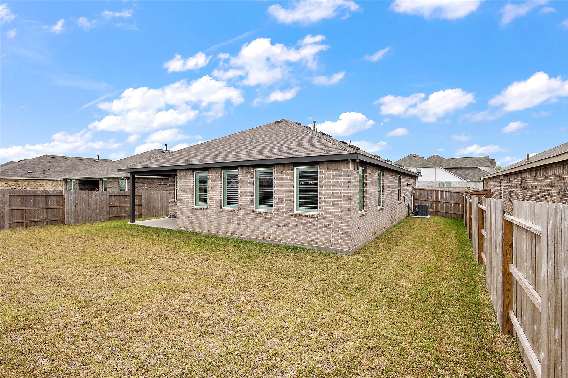 3414 Eden Valley Lane, Rosenberg, TX 77471 This photo shows the backyard of a brick house with a covered patio. The yard is fenced and has a grassy area, offering a private outdoor space.