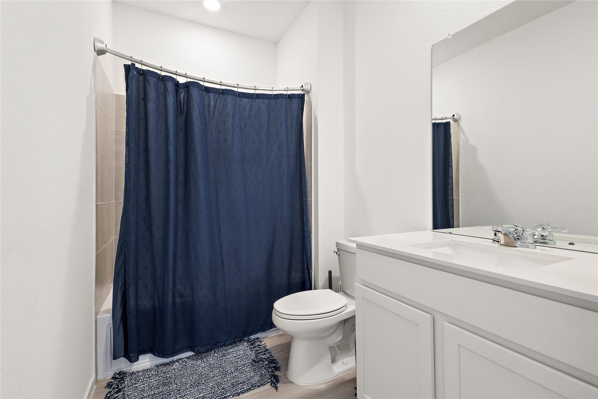 3414 Eden Valley Lane, Rosenberg, TX 77471 This bathroom features a clean, modern design with a white vanity, a large mirror, and a bathtub with a navy blue shower curtain. The space is well-lit with a minimalist aesthetic.