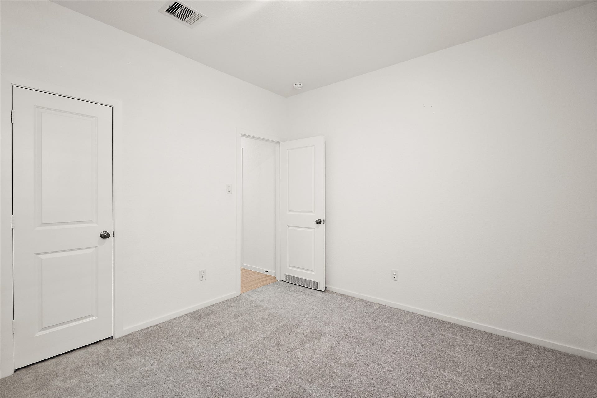 3414 Eden Valley Lane, Rosenberg, TX 77471 This photo shows a minimalist, unfurnished room with white walls, gray carpeting, and two white doors. Ideal for a bedroom or office space.