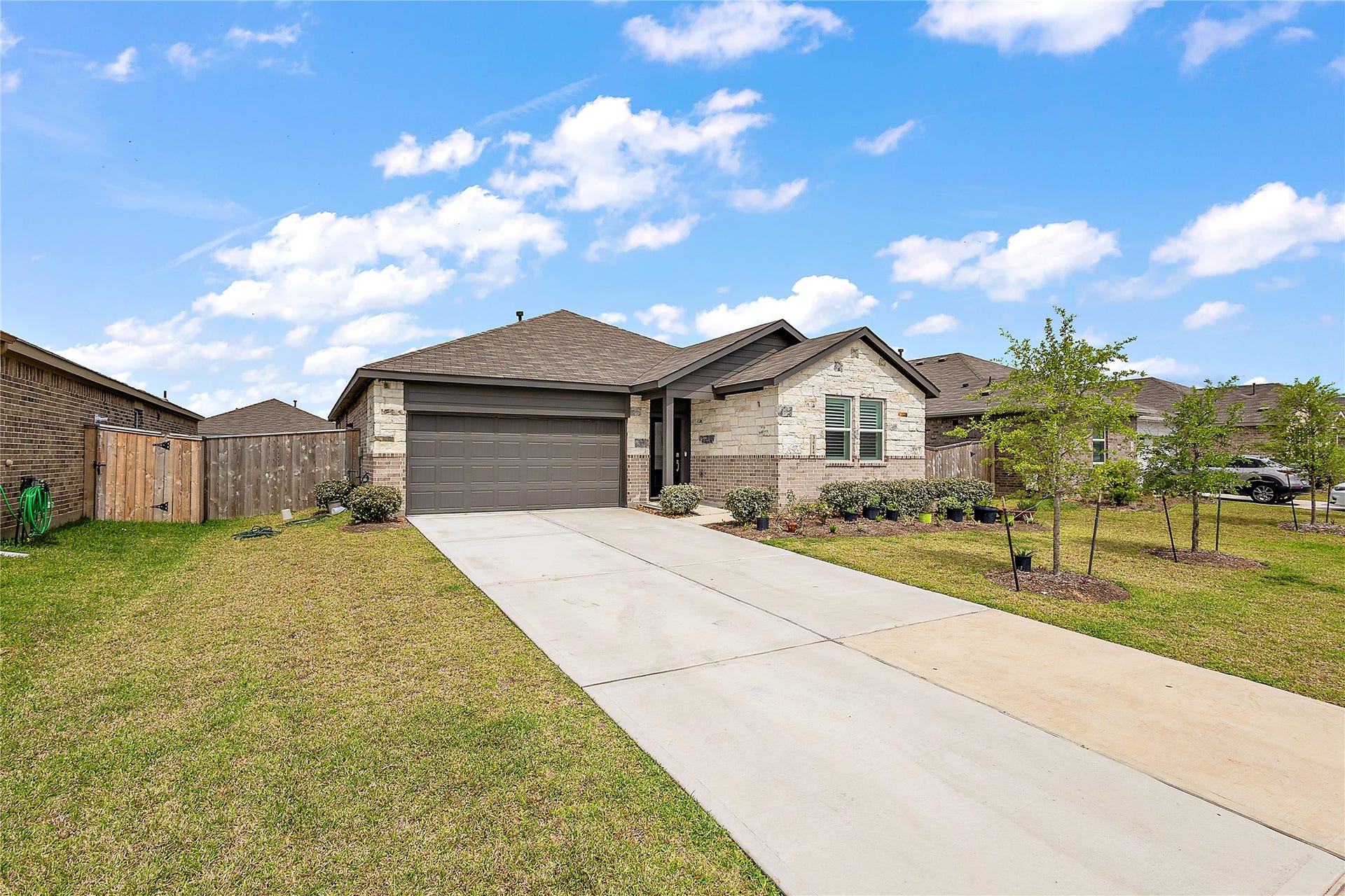 3414 Eden Valley Lane, Rosenberg, TX 77471 modern single-story home with a stone and brick exterior, featuring a two-car garage and a neatly landscaped front yard. The long driveway and well-kept lawn add to the curb appeal.