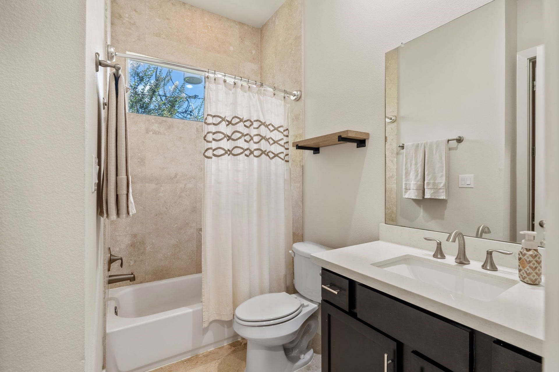 This bathroom has a vanity with quartz countertops, plenty of storage and a shower/tub combo.