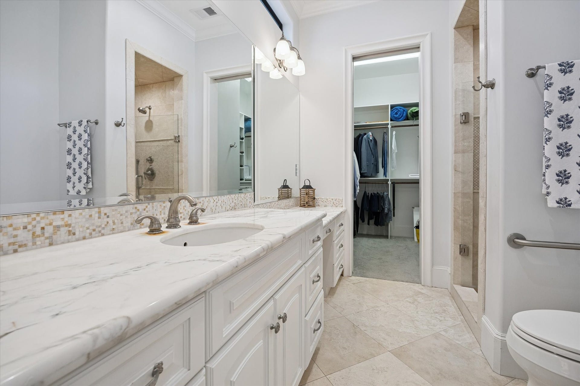 4022 Coleridge Street, West University Place, TX 77005 Ensuite bathroom serving the first-floor junior suite, featuring a walk-in shower, marble countertops, and generous storage. The adjacent walk-in closet adds even more convenience with abundant cabinetry and hanging space for wardrobe essentials.