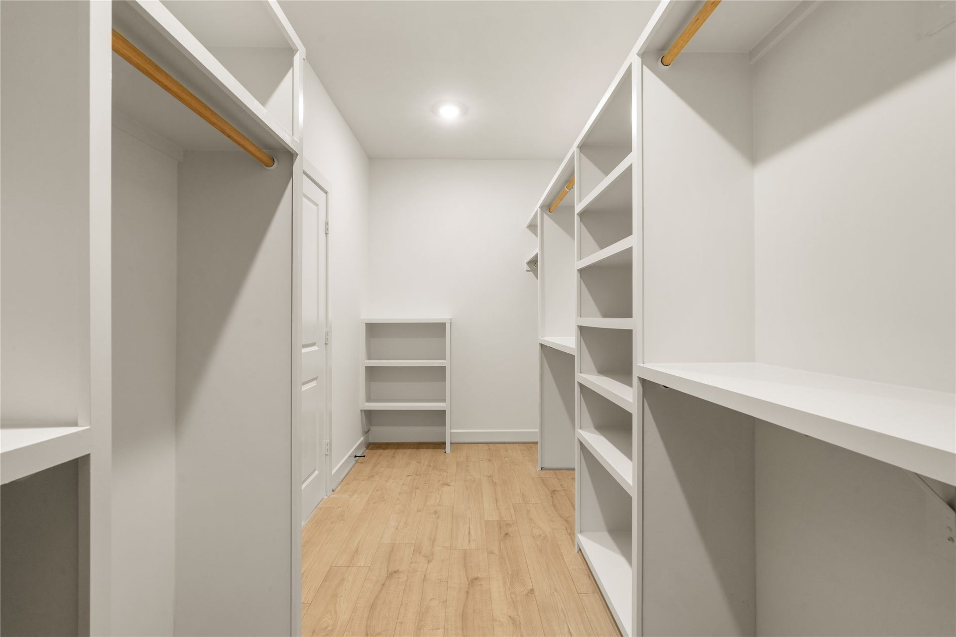 5016 Schuler Street, Houston, TX 77007 Expansive primary walk-in closet custom built-in shelving towers, shoe racks, and dual hanging rods set over warm wood-look floors.