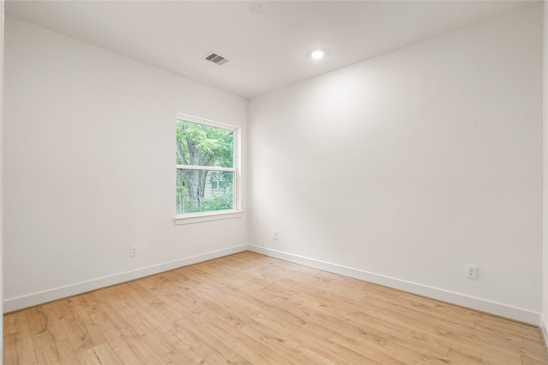 5016 Schuler Street, Houston, TX 77007 Quiet corner bedroom warm oak-look flooring, window overlooking mature greenery, and clean neutral paint finishes.