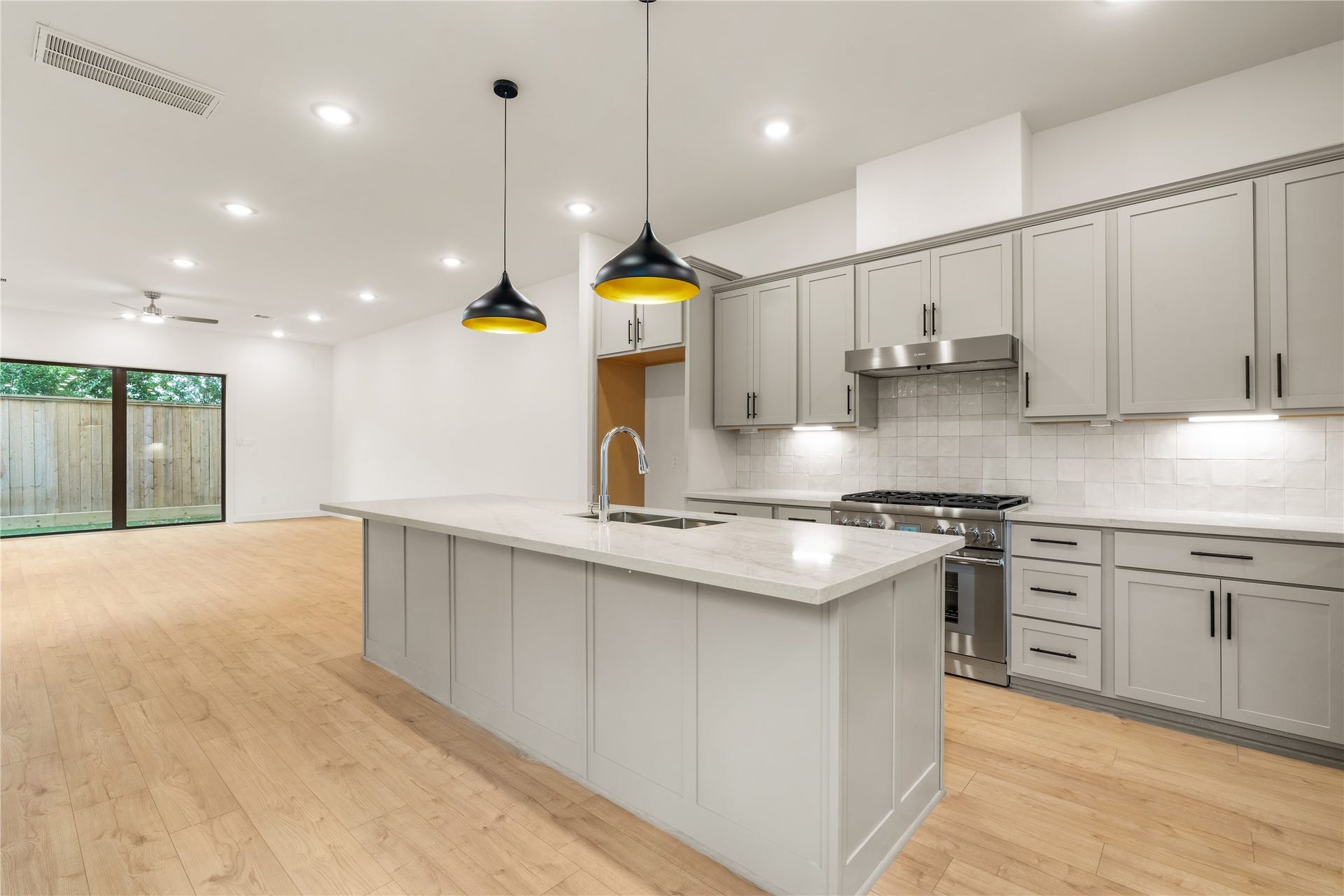 5016 Schuler Street, Houston, TX 77007 Chef's kitchen perspective massive quartz island with bar seating potential, statement matte black and gold pendant lighting, gas cooktop setup, and soft grey shaker cabinetry extending to the main floor living space.
