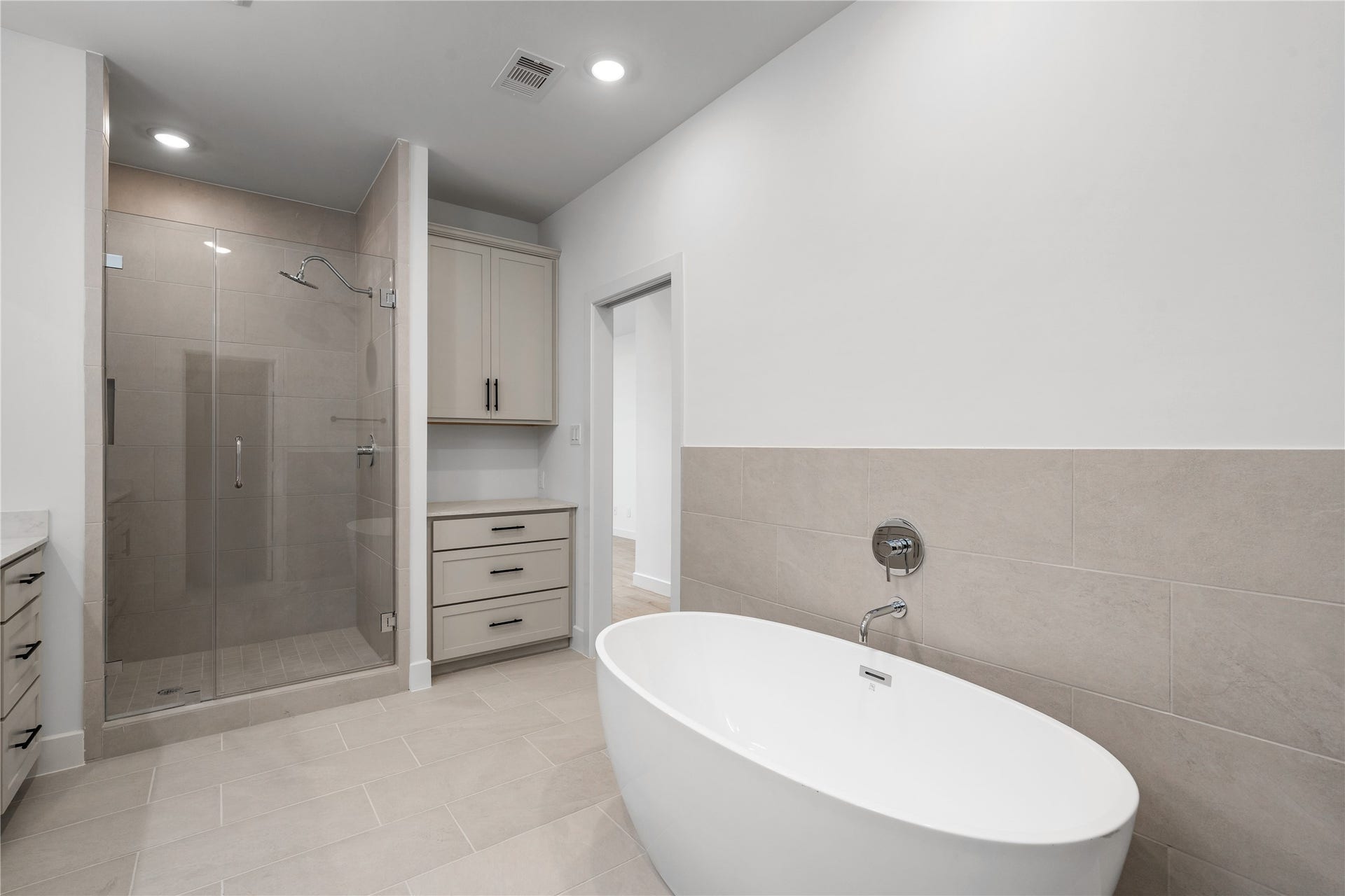 5016 Schuler Street, Houston, TX 77007 Primary bathroom oasis freestanding soaking tub set against tile wainscoting, walk-in tile shower, and built-in storage drawers.