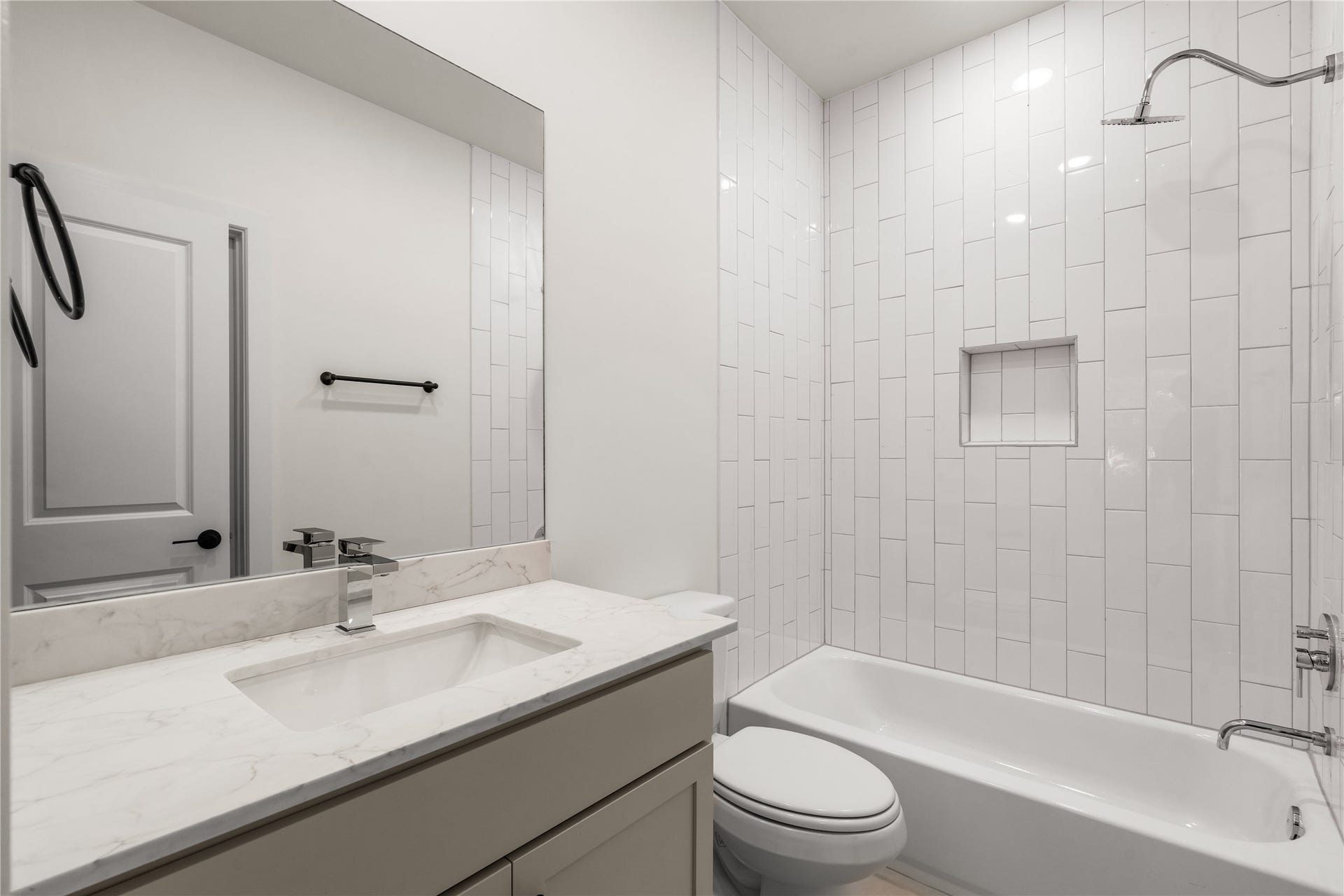 5016 Schuler Street, Houston, TX 77007 Guest bath setup vertical stack subway tile surround, built-in shampoo niche, quartz-topped vanity, and clean black hardware accents.