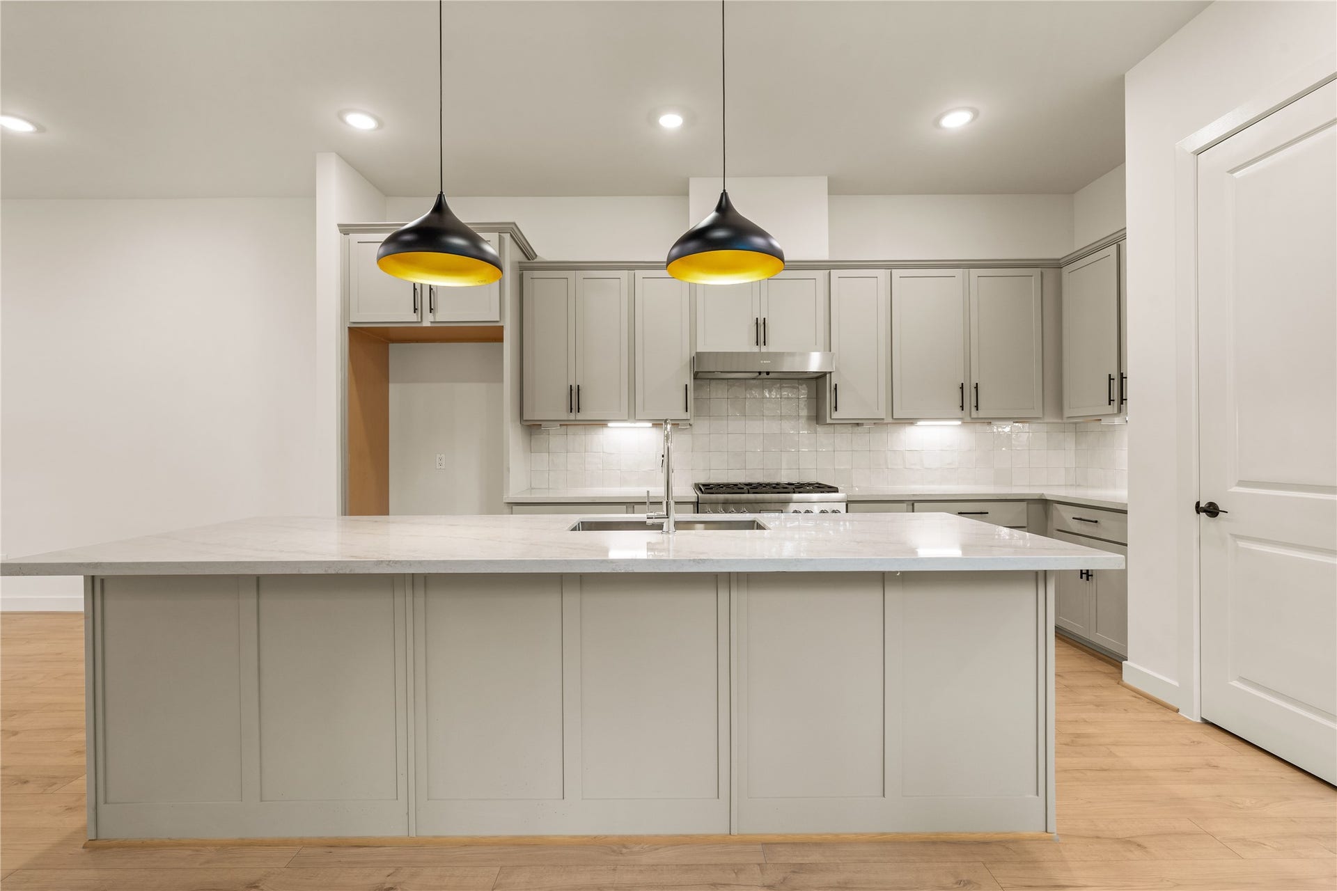 5016 Schuler Street, Houston, TX 77007 The culinary center expansive quartz prep island with undermount double sink, stainless steel range hood, under-cabinet lighting, and clean tile backsplash.