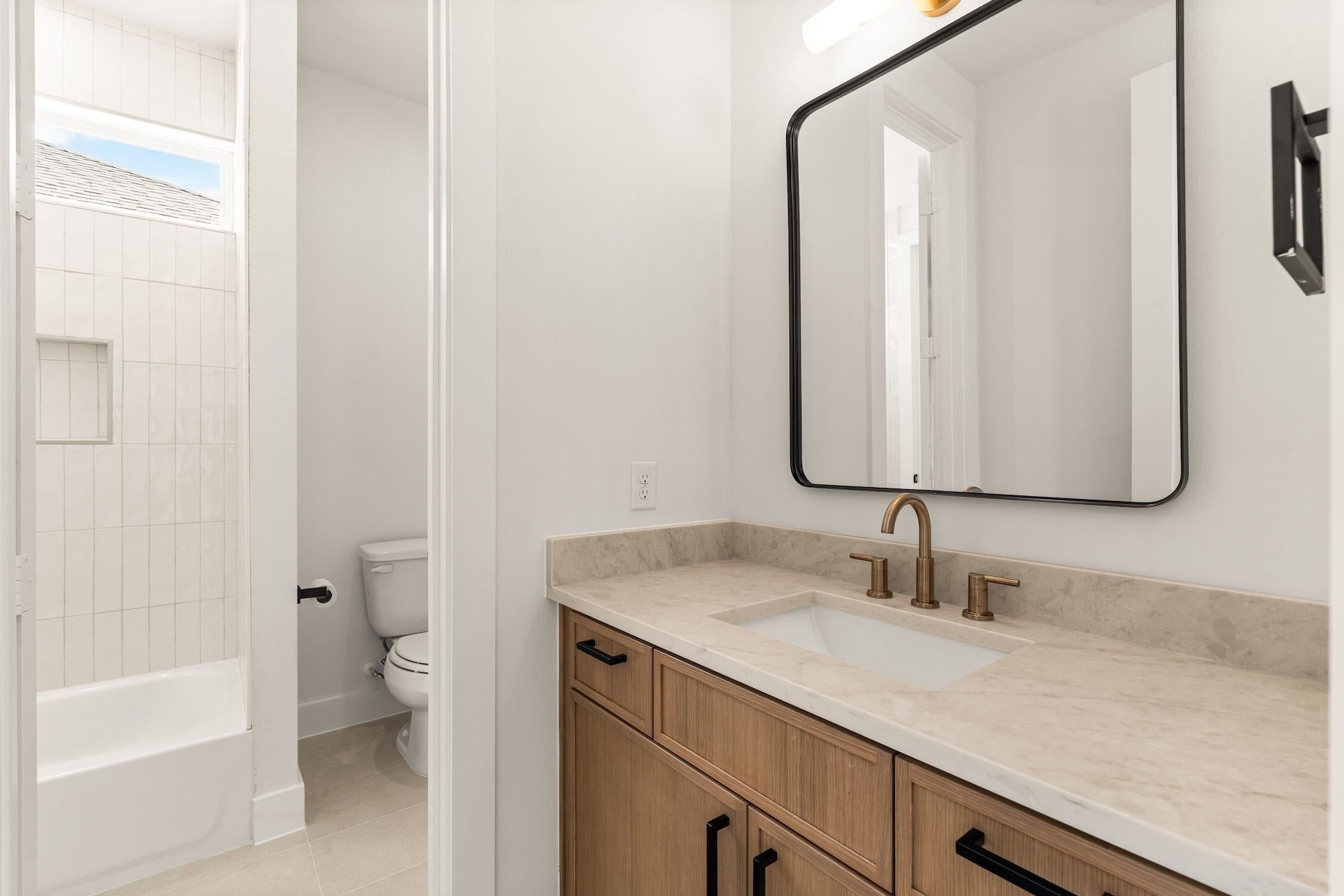 Full secondary jack and jill bathroom with a modern vanity, warm brass accents, and custom tile surround.
