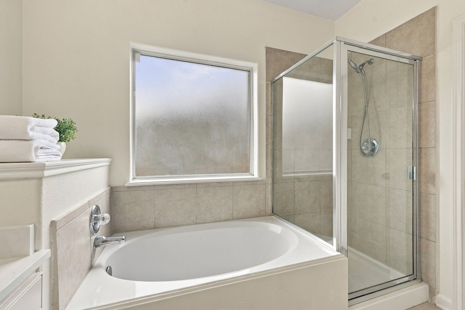 The shower features a neutral tile surround, complemented by a chrome handheld shower wand and coordinating fixtures for a clean, timeless look.