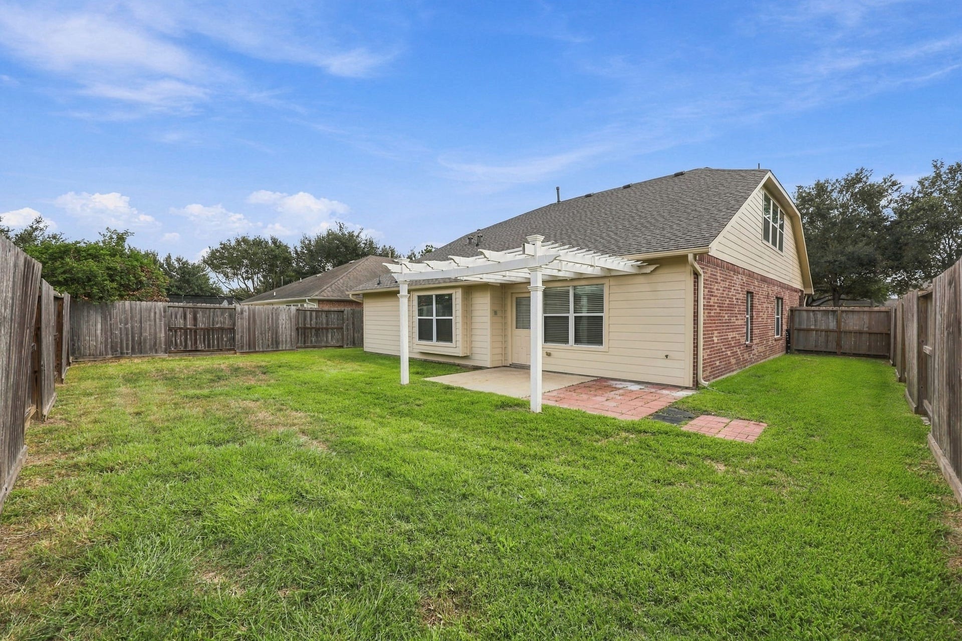 This rear view showcases the back of the home, the inviting pergola, spacious additional side yard, and newly installed roof. The generous outdoor space offers plenty of potential for relaxing, entertaining, and creating your ideal backyard retreat.