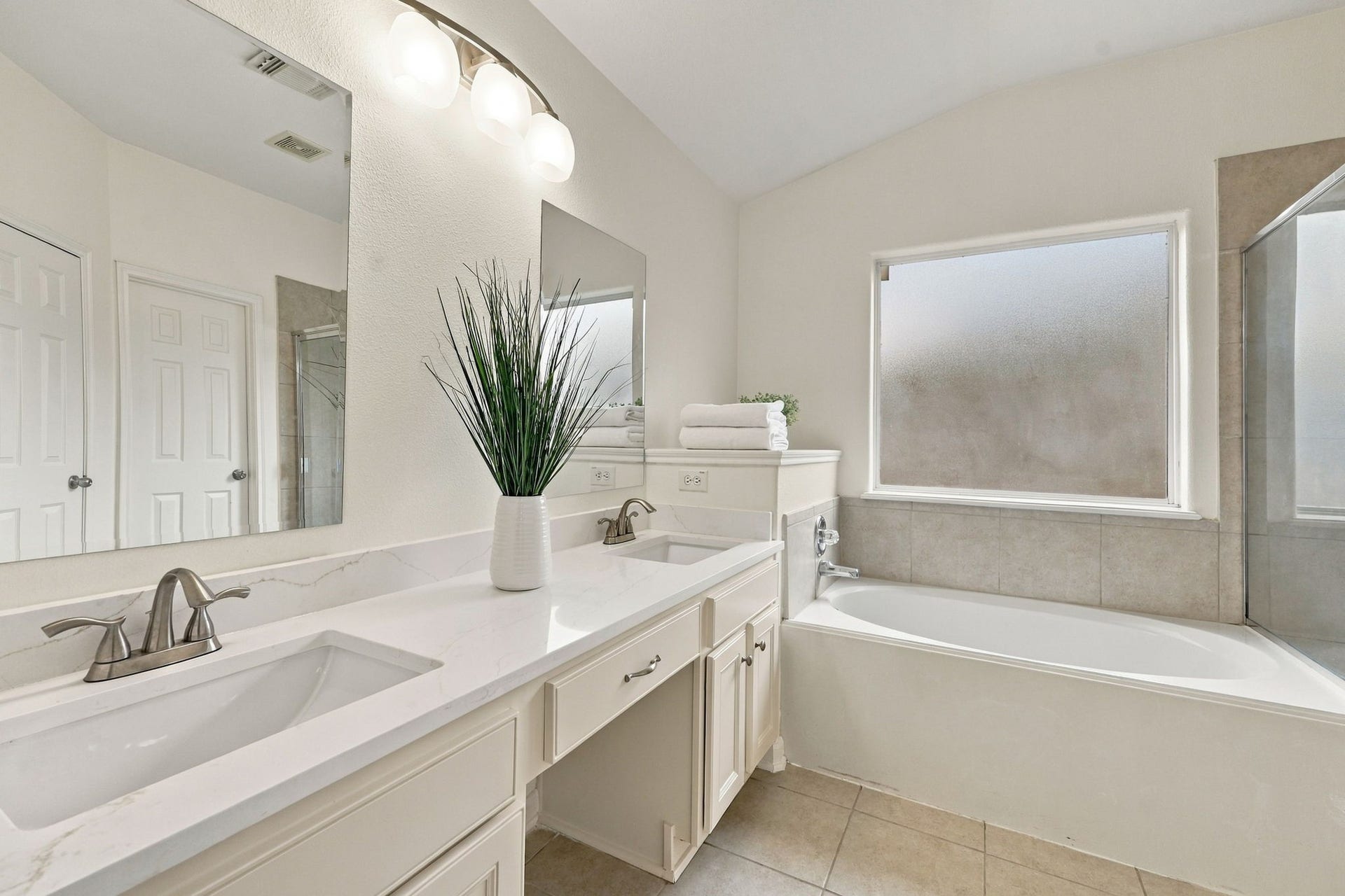 The Primary Bath features newly painted cabinetry, Quartz countertops, and double undermount sinks with brushed nickel faucets. A coordinating light fixture completes the refreshed and updated look.