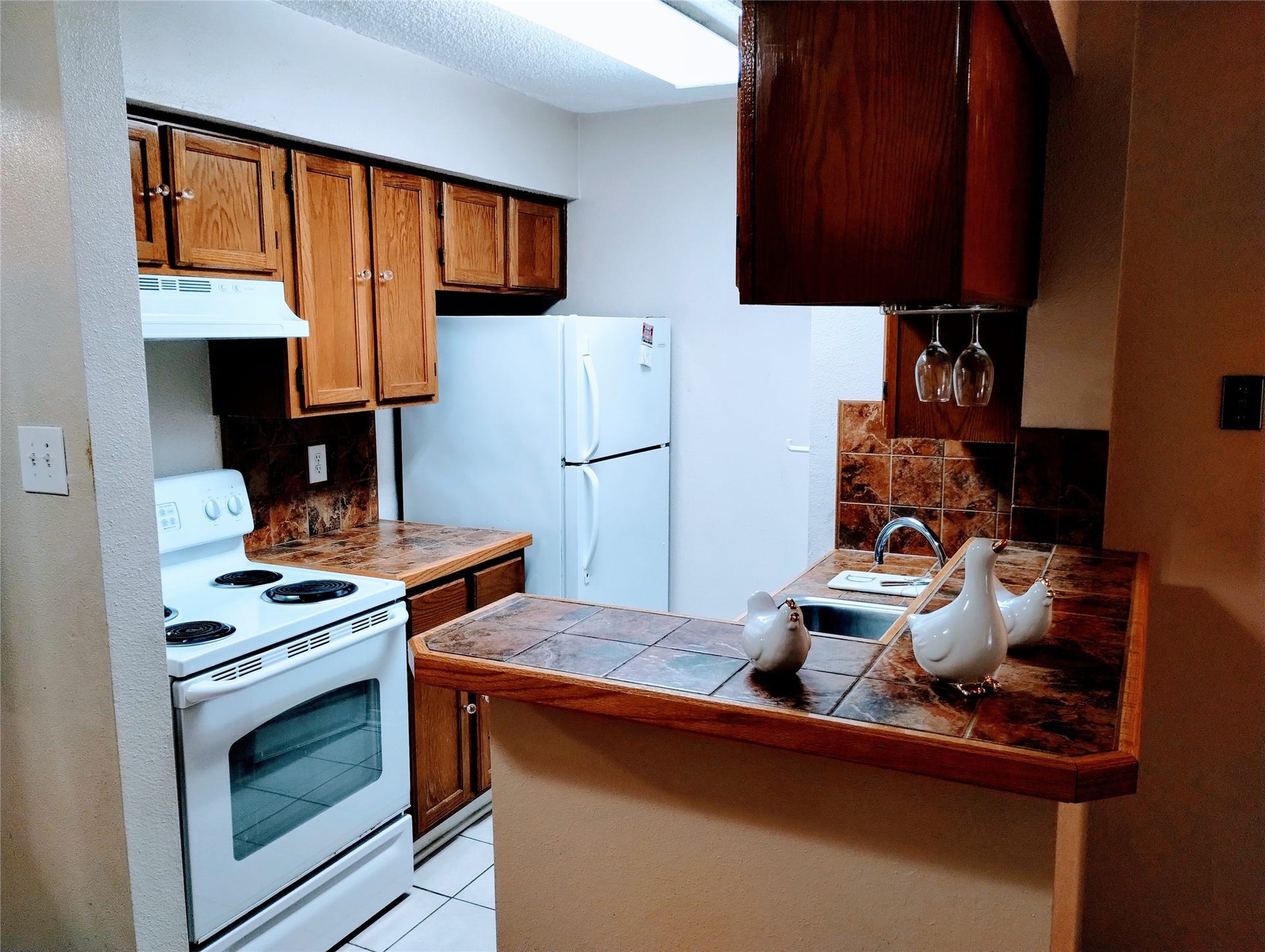 11201 Lynbrook Drive, #3807, Houston, TX 77042 The charming KITCHEN has ample cabinetry, tiled countertops, and white appliances including a refrigerator, electric range with a vent hood, and a dishwasher.