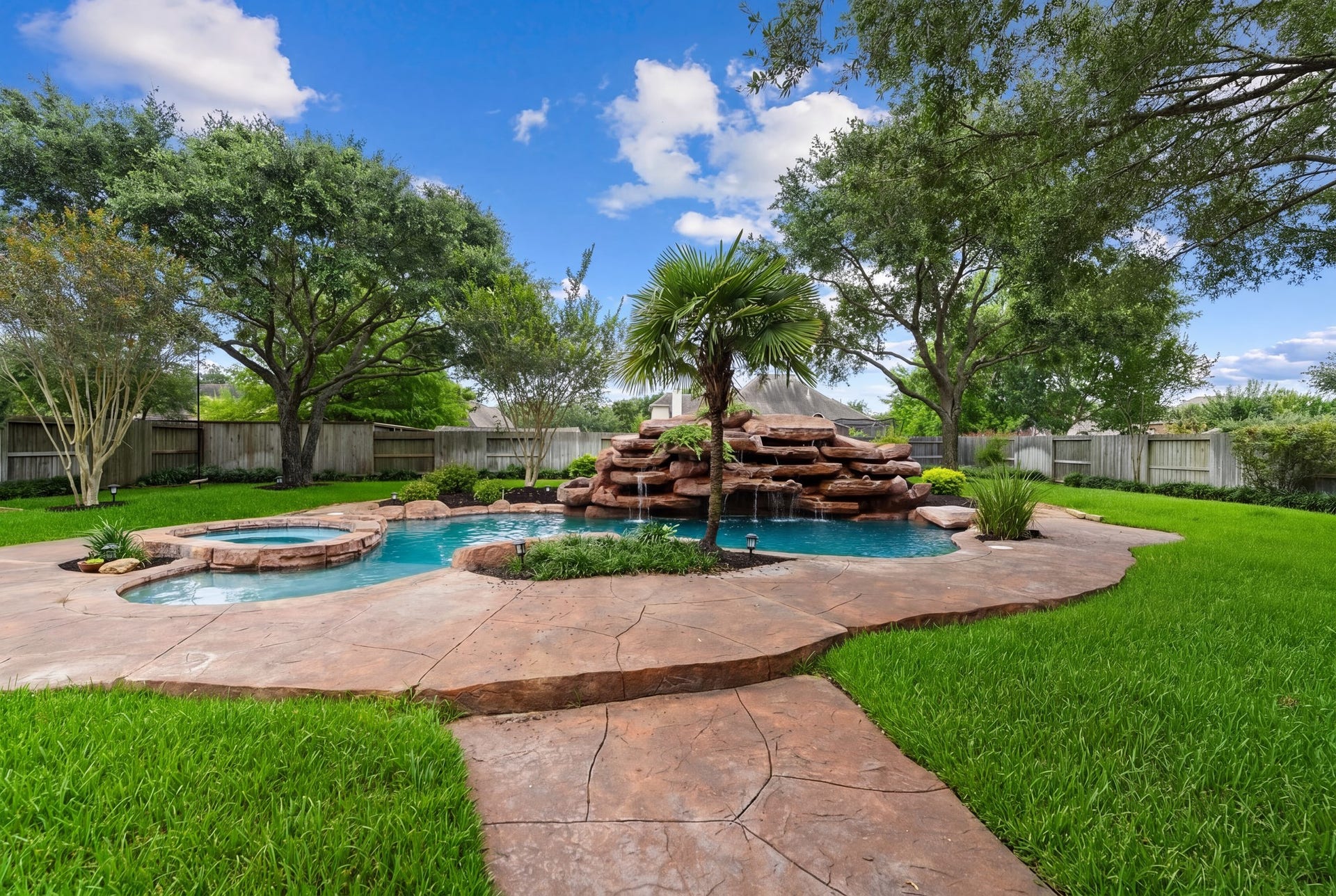 The heated in-ground pool and spa create a resort-style setting with rock accents, a waterfall feature, and peaceful green surroundings.
