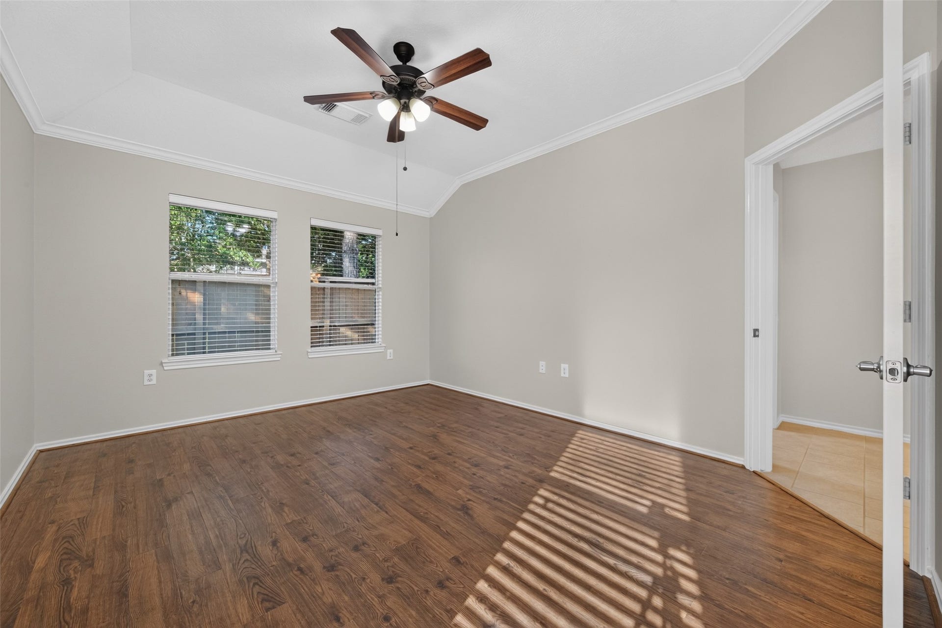 The primary bedroom features beautiful fresh neutral paint, wood flooring, elegant crown molding, a ceiling fan, and two windows that bring in natural light, creating a warm and inviting retreat.