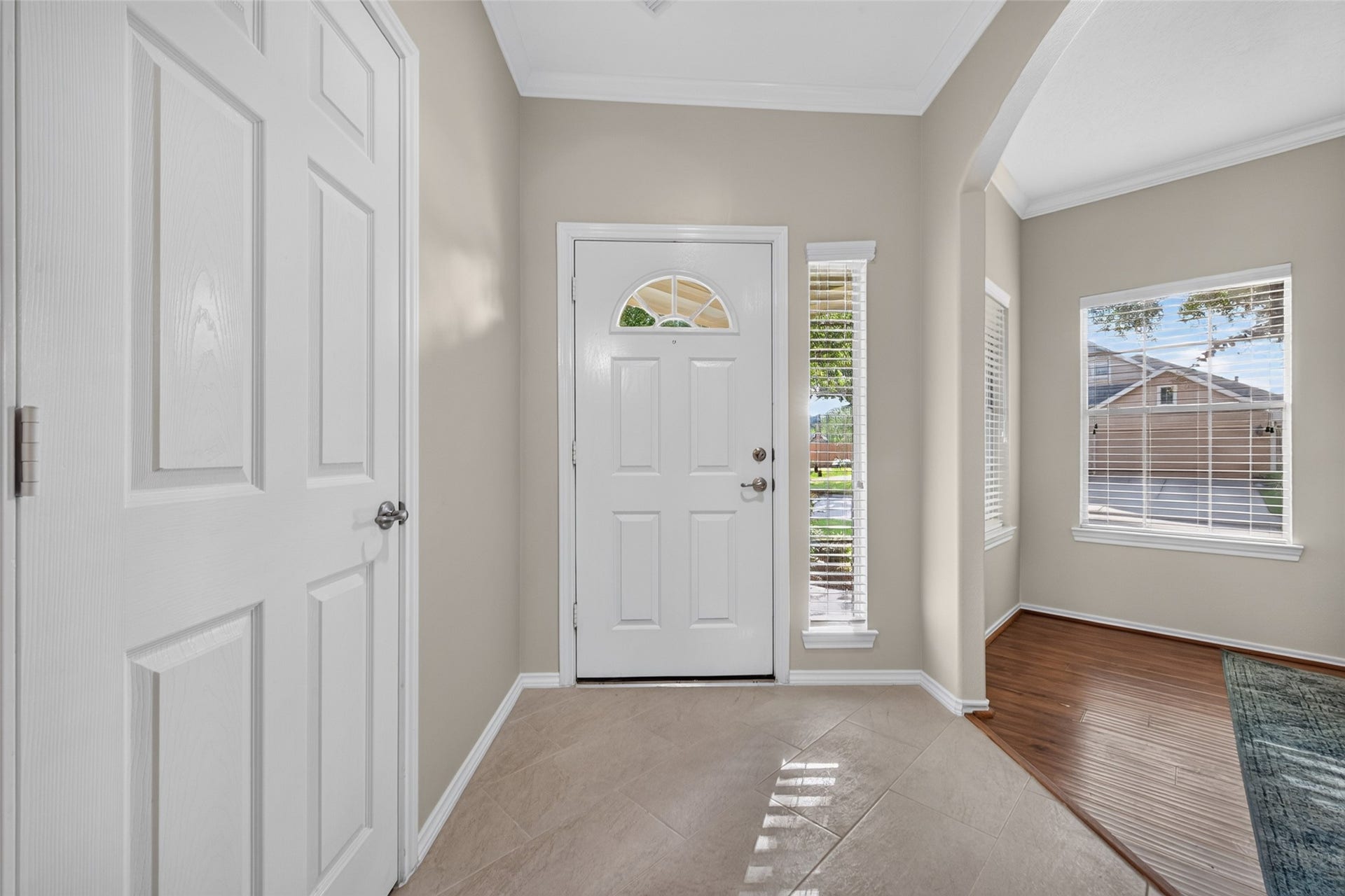 A warm, welcoming entryway featuring BRAND NEW tile flooring, FRESH INTERIOR PAINT, crown molding, and a graceful archway leading into a room with beautiful hardwood floors.