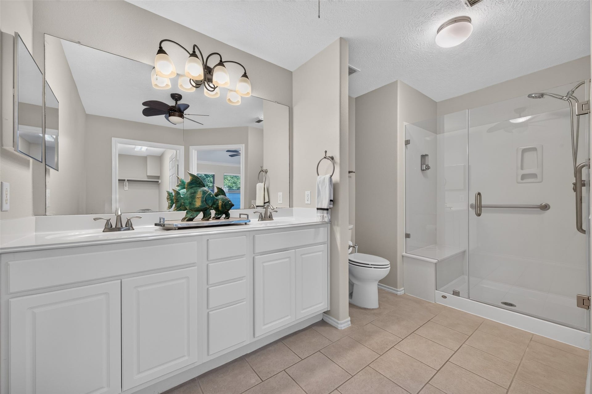 The primary bathroom features a double-sink vanity with generous cabinet storage, a large mirror, and a walk-in shower with glass doors, built-in seating, and grab bars for added safety and comfort.