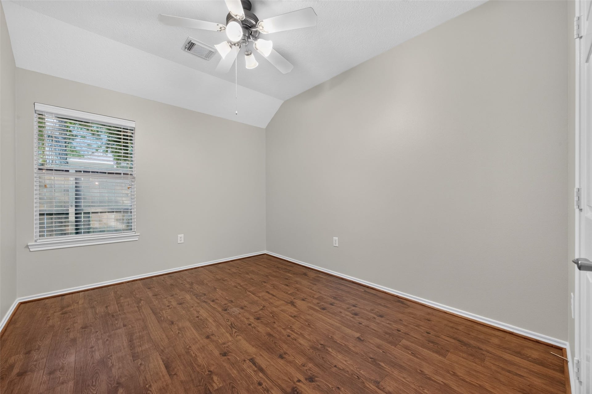 The guest bedroom features beautiful hardwood floors, a vaulted ceiling, ceiling fan, and a window bringing in natural light.
