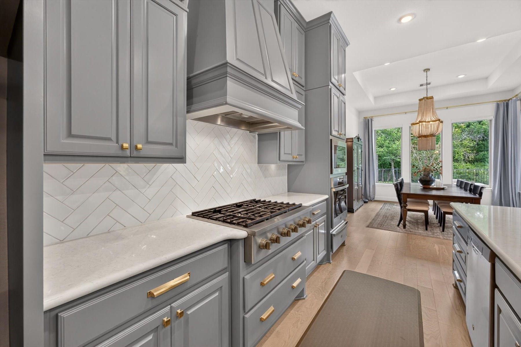 1219 Mcmurtry Ridge Drive, Katy, TX 77494 Elegant chefs kitchen featuring custom cabinetry, quartz countertops, a striking herringbone backsplash, and a professional-style gas range with coordinating gold hardware.