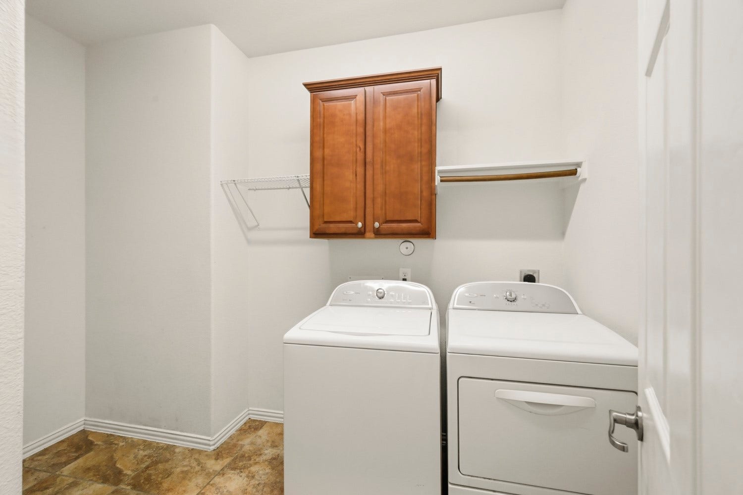 This spacious utility room features full washer and dryer hookups, a built-in wall cabinet for hidden detergent storage, open hanging racks and shelving for air-drying clothes.