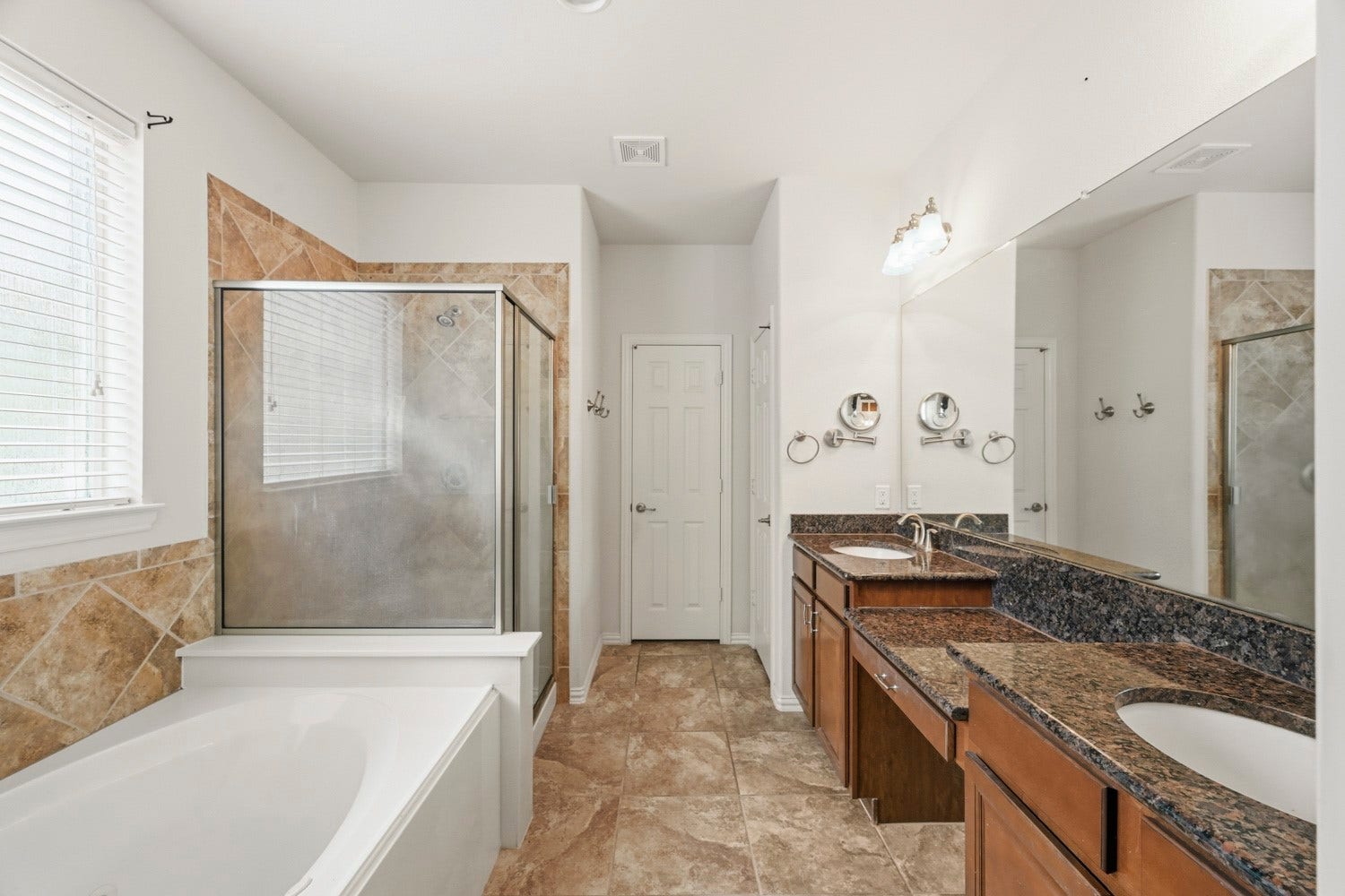 This generous primary bath offers a retreat-like atmosphere with plenty of functional space. Enjoy dual sinks, granite surfaces, a dedicated vanity station, durable tile flooring, and a glass shower alongside a deep soaking tub.