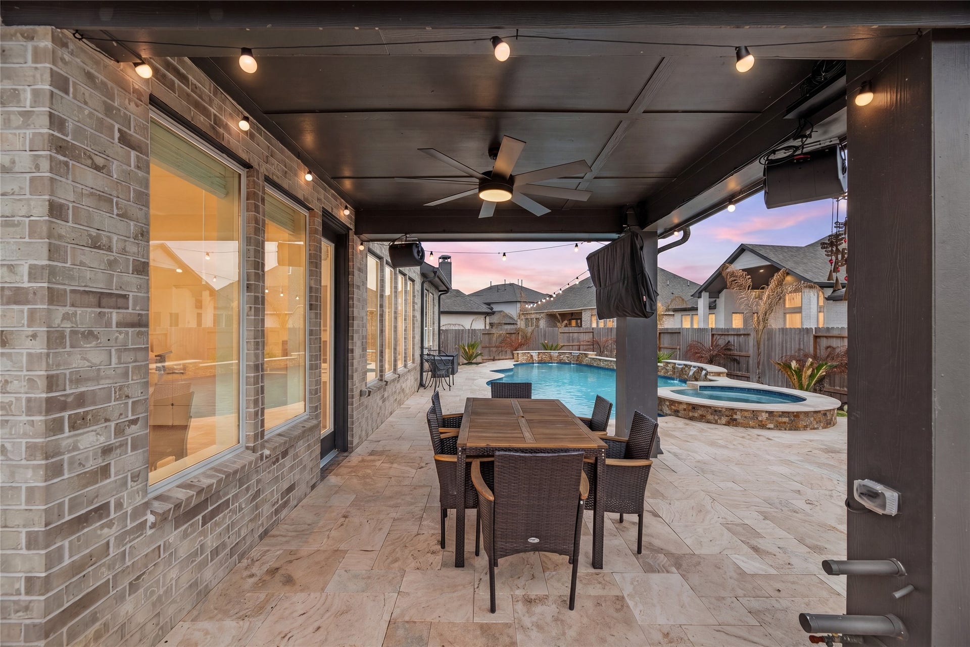 Designed for year-round enjoyment, this covered outdoor living space features a spacious dining area, ceiling fan, and ambient string lighting overlooking the backyard oasis. Seamlessly connected to the home and just steps from the pool and spa, it's an ideal setting for outdoor dining, entertaining, or relaxing evenings at home.