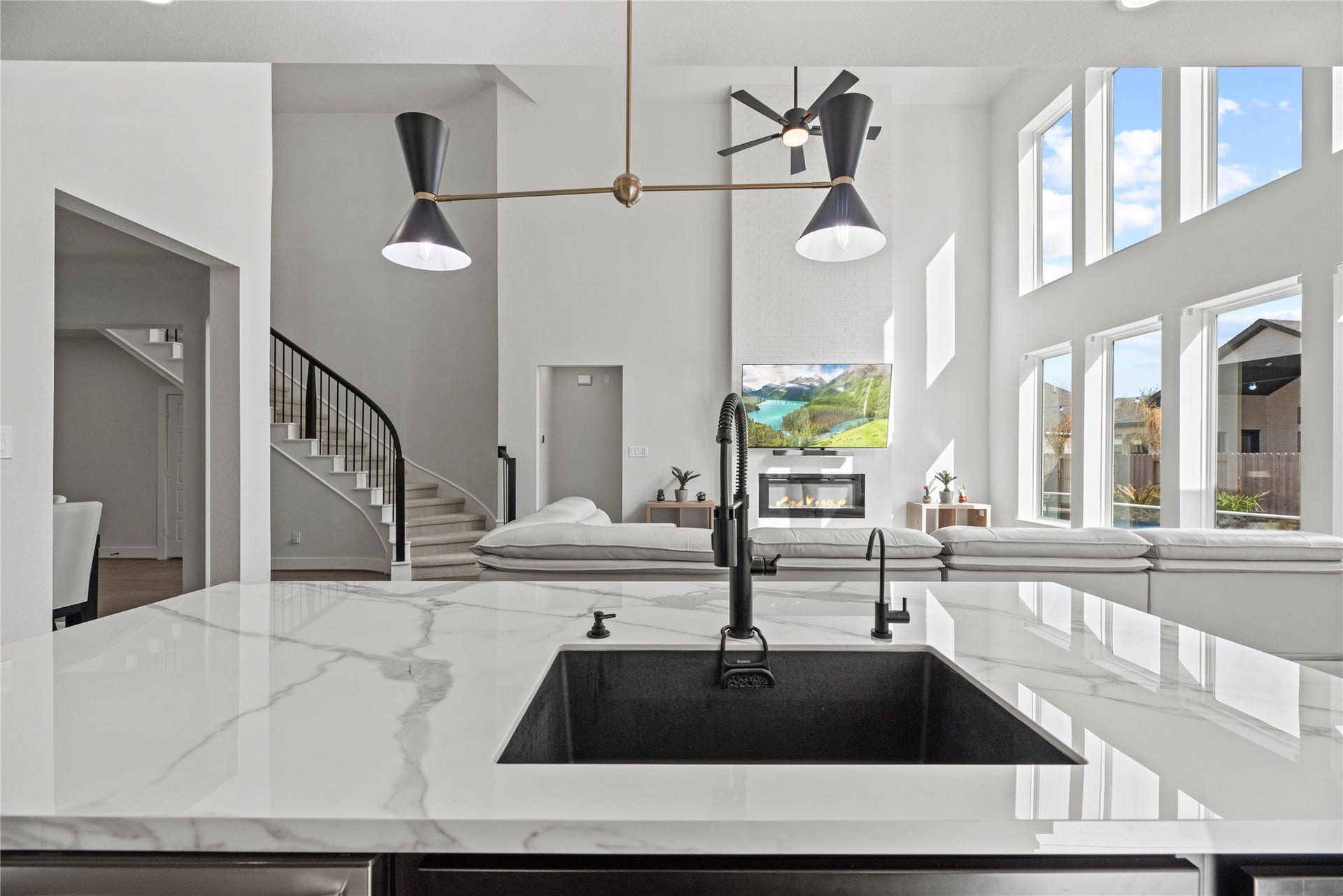 Stunning open-concept design highlighted by a dramatic two-story living room, floor-to-ceiling windows, and a sleek fireplace feature wall. The oversized quartz island with a modern undermount sink and statement lighting overlooks the living spaceperfect for entertaining while enjoying views of the backyard and pool.