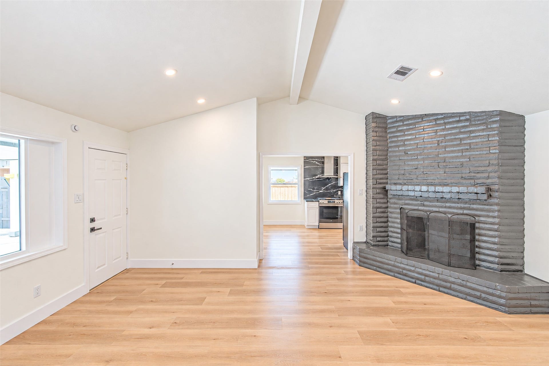 Bright and inviting living space featuring vaulted ceilings, elegant wood flooring, and a striking brick fireplace.