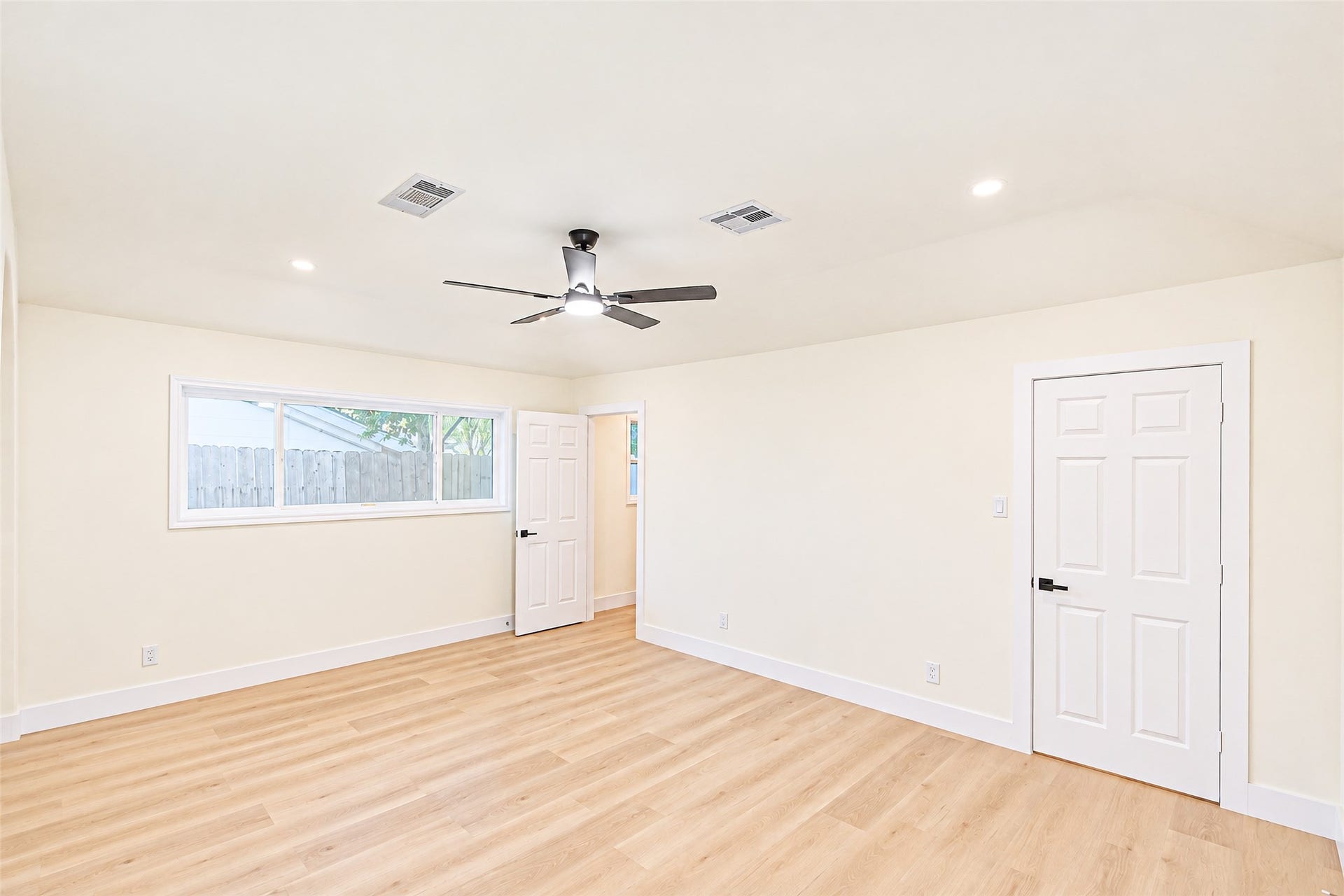 Spacious and bright, the primary bedroom features sleek wood flooring, a modern ceiling fan, and ample natural light, creating a serene retreat.
