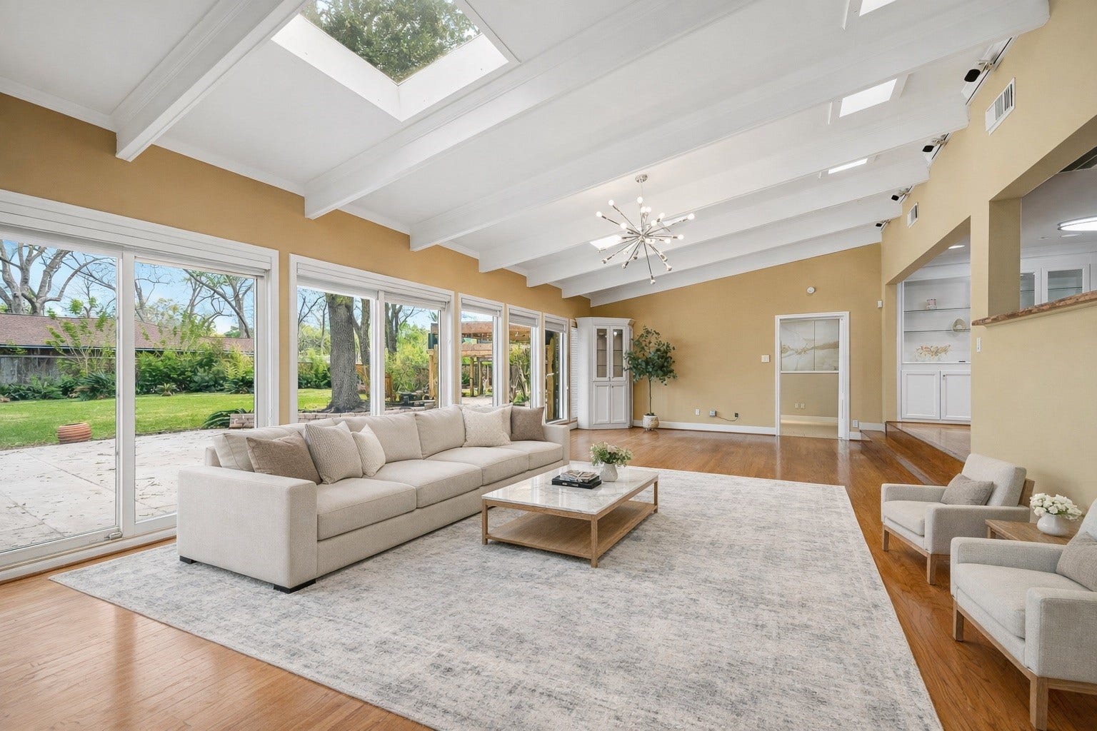 2111 N Galveston Avenue, Pearland, TX 77581 Virtual Stage - White beam ceilings with skylights create a bright, airy, and luxurious atmosphere. Large glass doors showcase stunning backyard views, while rich brown hardwood floors add warmth and elegance to the space.