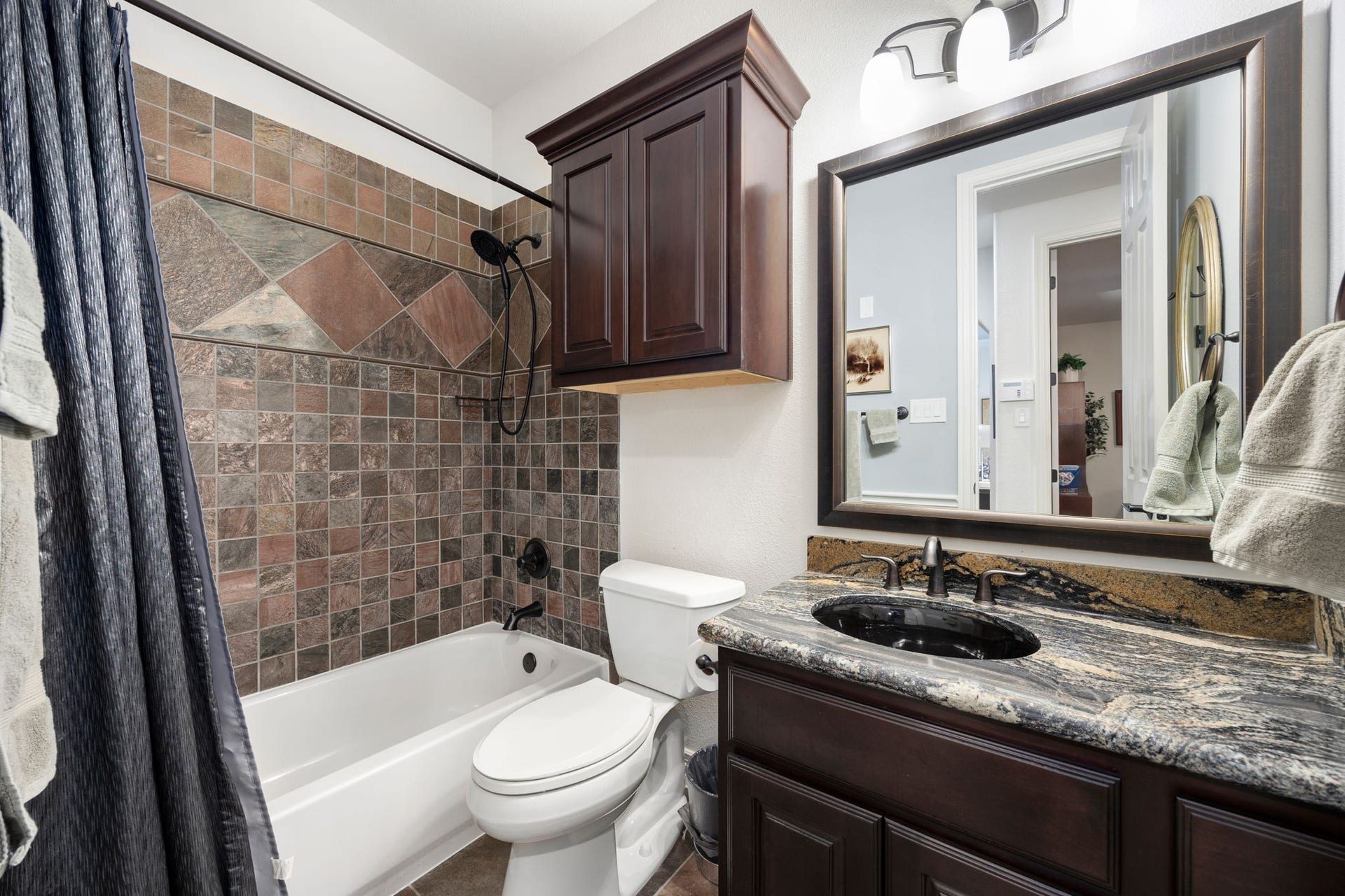 195 Oarwood Place, The Woodlands, TX 77389 Beautiful secondary bathroom with granite countertops, custom cabinetry, and a shower/tub combination with stylish tile. A built-in storage cabinet provides extra space for towels and essentials.