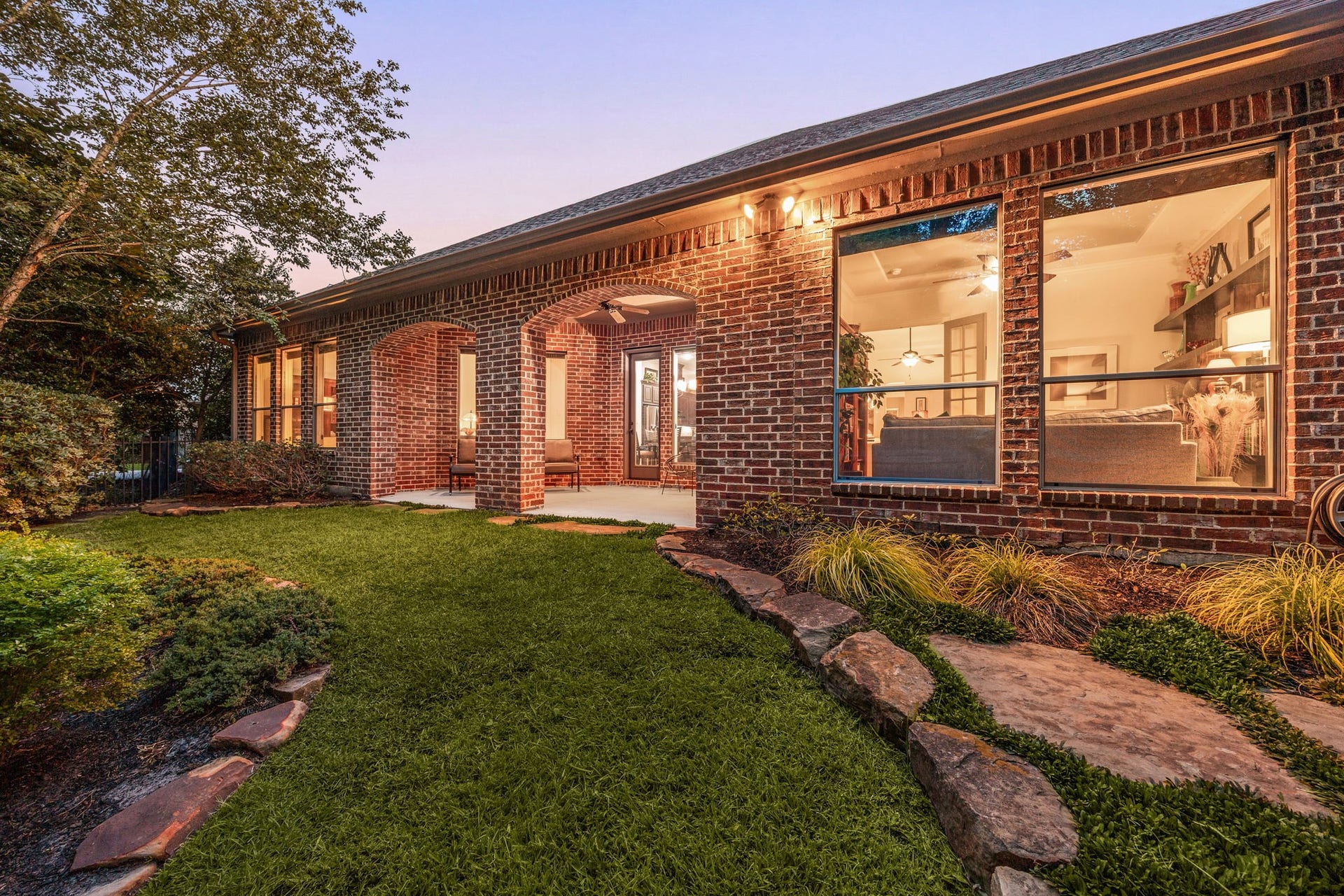 195 Oarwood Place, The Woodlands, TX 77389 This stunning wide-angle view highlights the incredible scale and warmth of the homes rear estate at dusk. Framed by timeless full-brick architecture, the property features sprawling walls of glass that cast a warm, inviting glow across the lush green lawn and custom natural flagstone pathways.